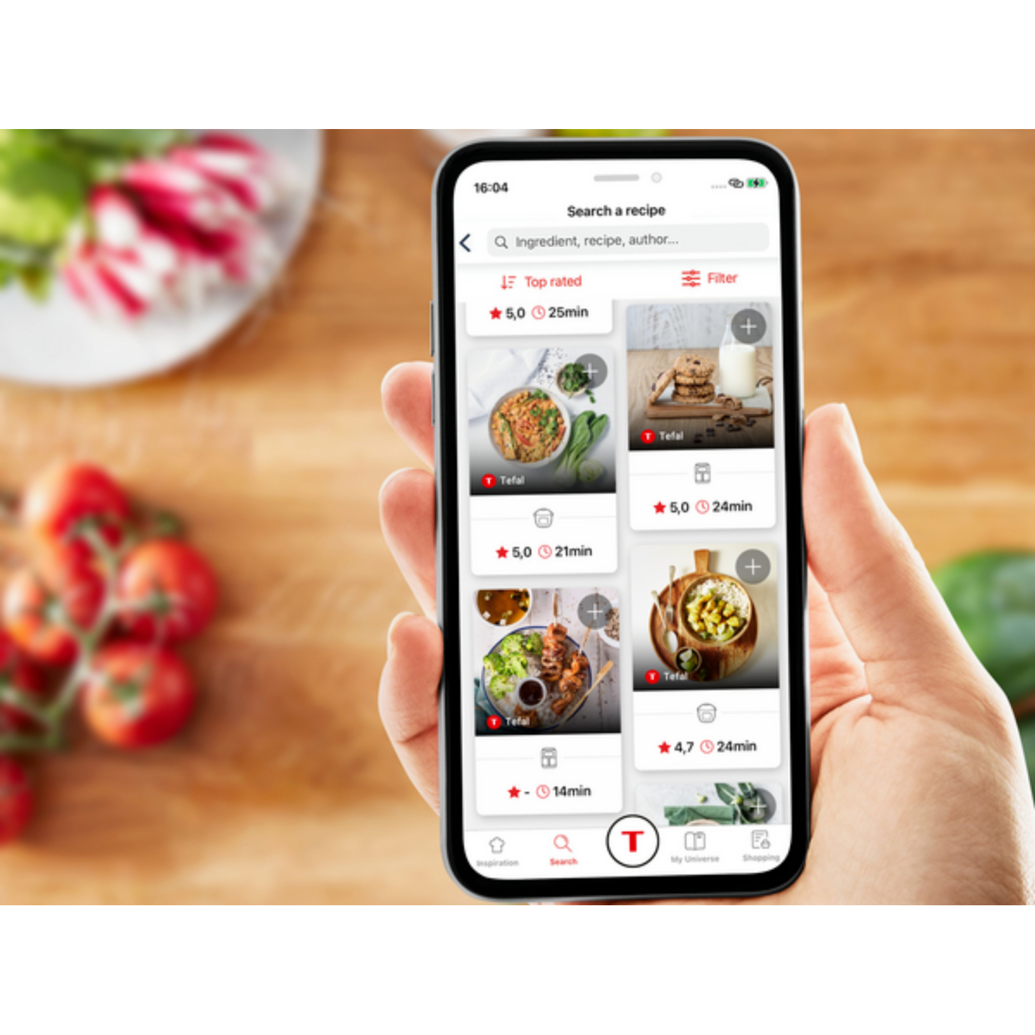A hand holding a smartphone displaying a recipe search app, with food items visible.
