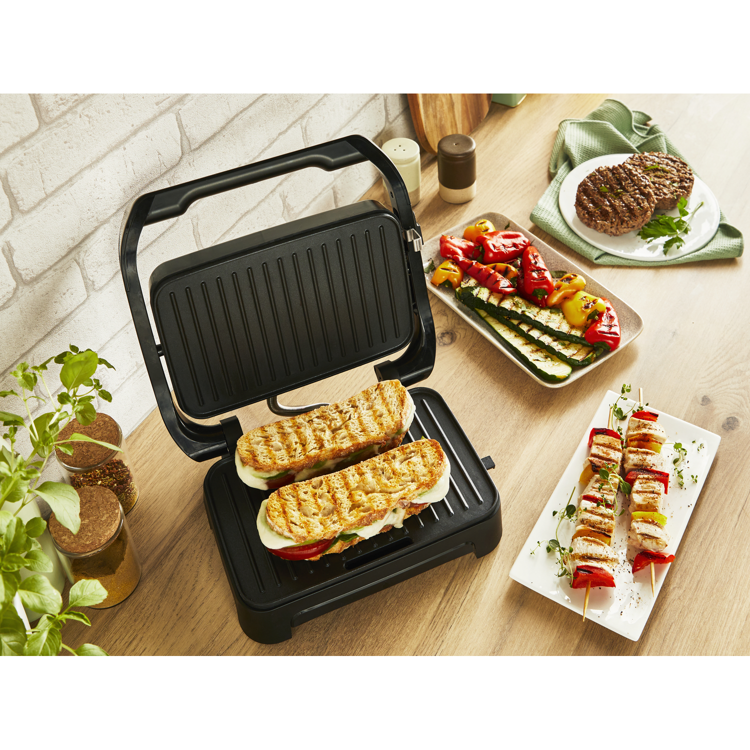 Zwarte grill met sandwiches, gegrilde groenten en spiesjes op een houten tafel.