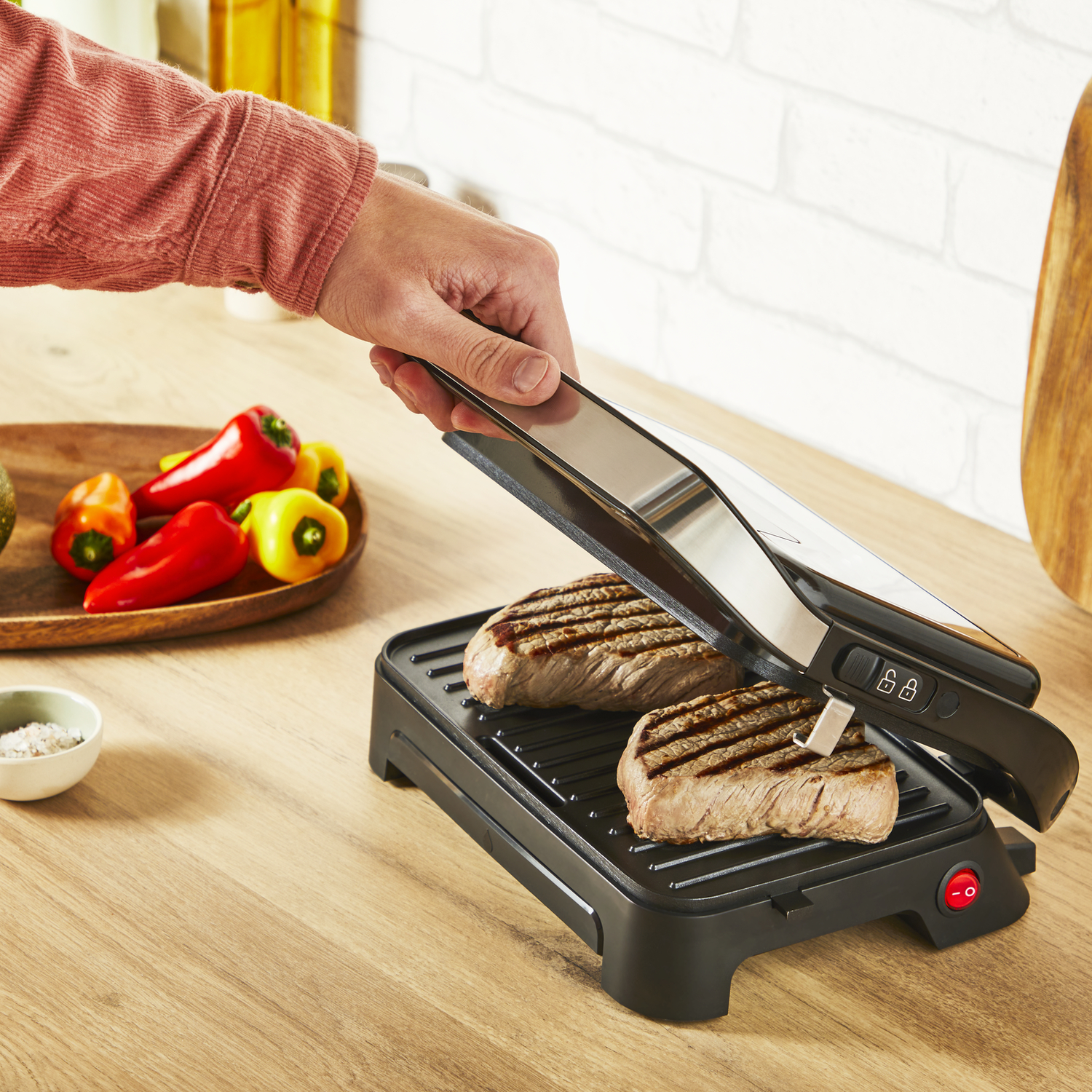 Biefstukken worden gegrild op een zwarte grill. Een hand houdt een tang vast om een biefstuk om te draaien.