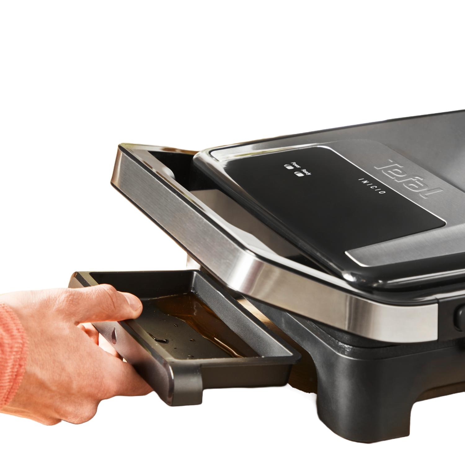 A person's hand is pulling out the oil tray from a black and silver electric grill, close-up shot.