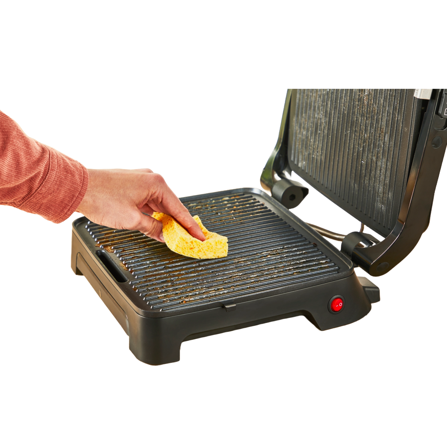 A person cleaning a dirty grill with a yellow sponge. The grill is on a black surface.