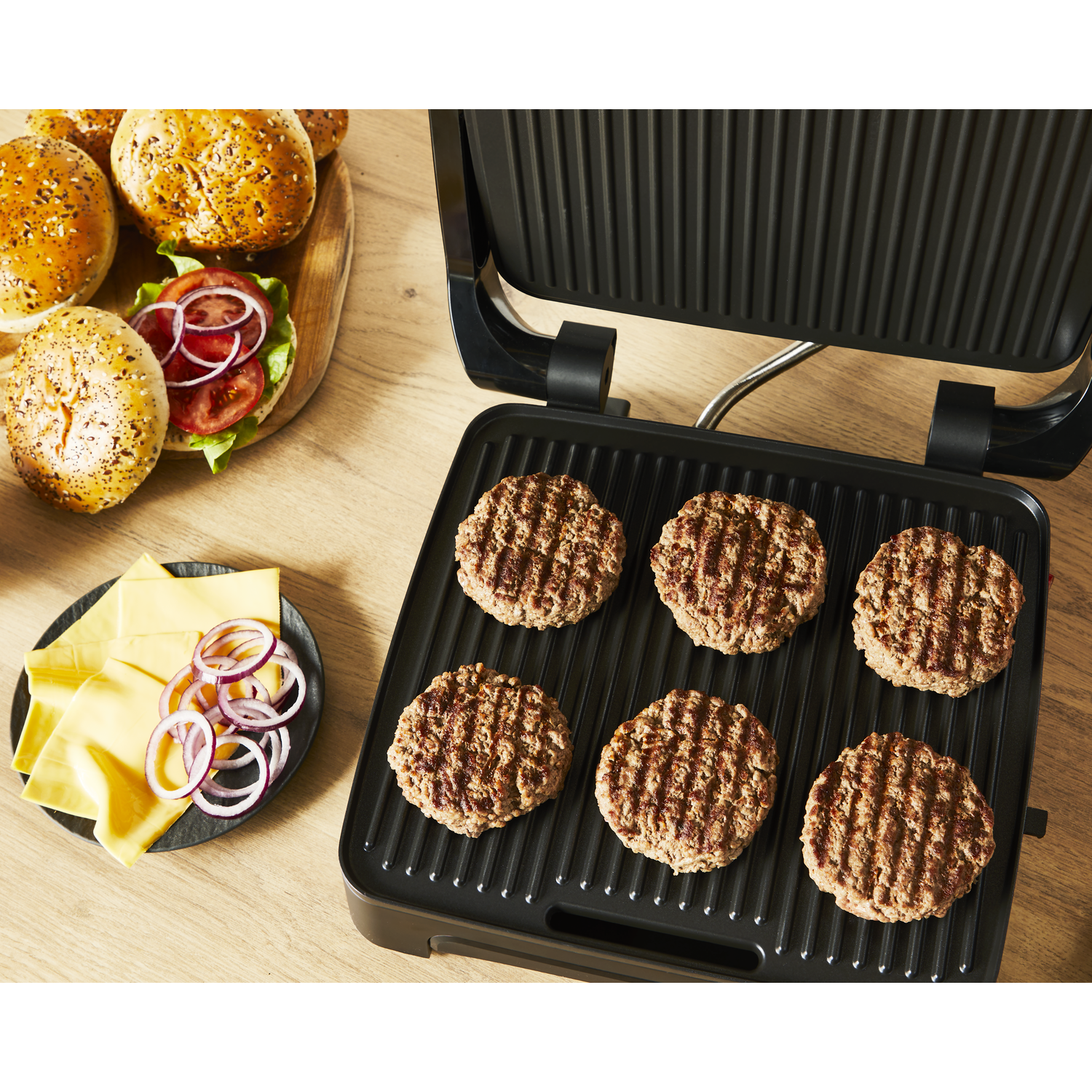 Grill with six cooked burgers. Ingredients like buns, cheese, and onions are on the side.