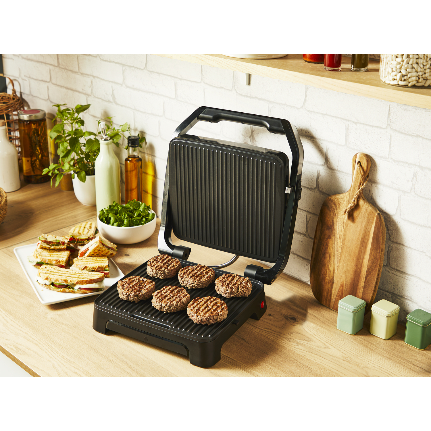 Black grill with cooked burgers. Food on plate. Kitchen setting with wood and green jars.