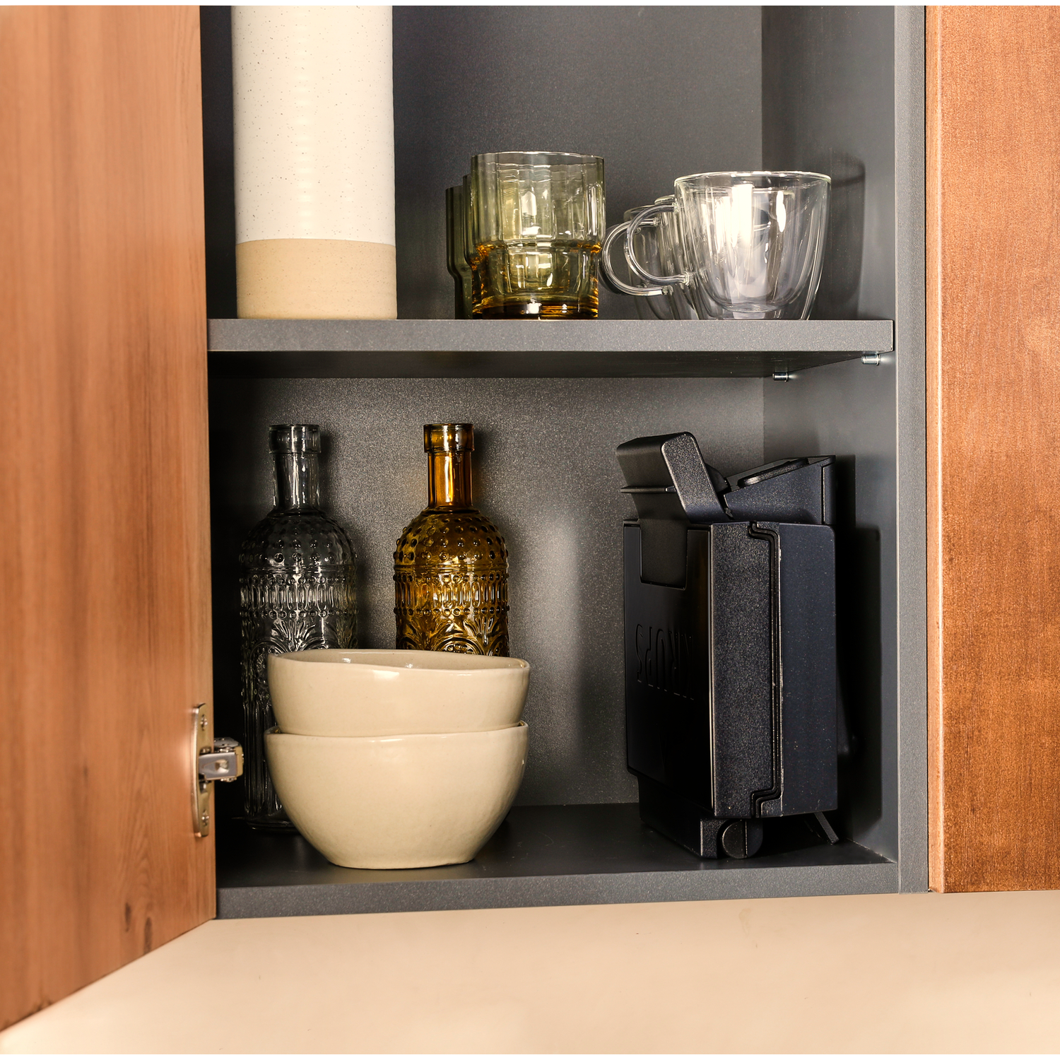 A cabinet shelf with jars, bowls, and a black device.