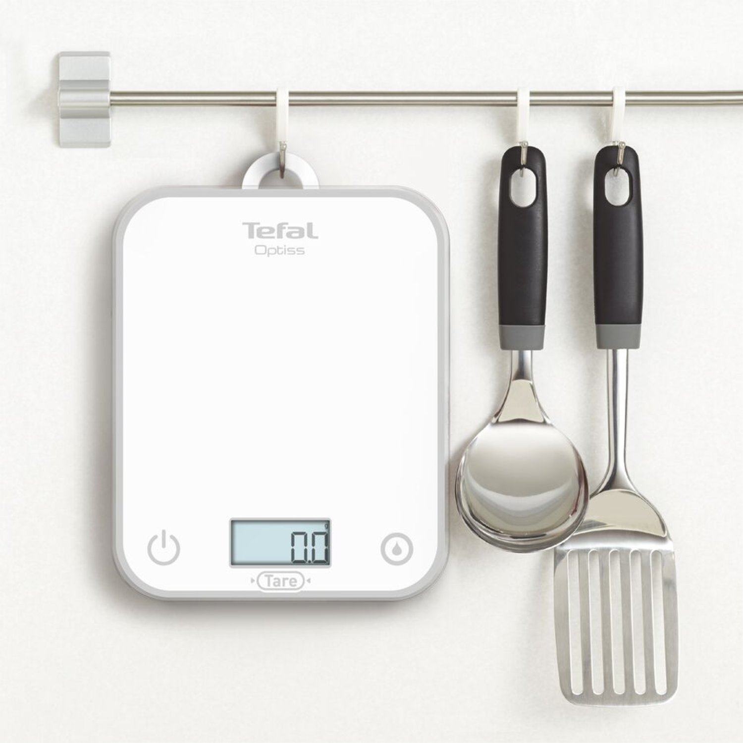 A white Tefal Optiss scale with a digital display of 0.0, and kitchen tools hanging on a metal bar.
