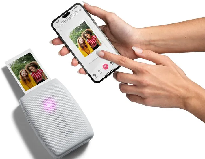 Un téléphone affiche une photo en cours d'impression par une imprimante portable. Deux mains sont visibles. L'imprimante émet une lumière rose.