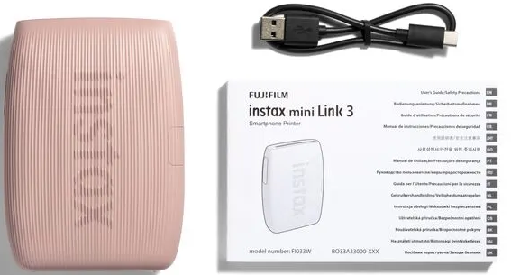 Une imprimante rose Instax Mini Link 3, un câble USB et un guide de l'utilisateur sont sur une surface blanche. Le logo de l'imprimante est visible.