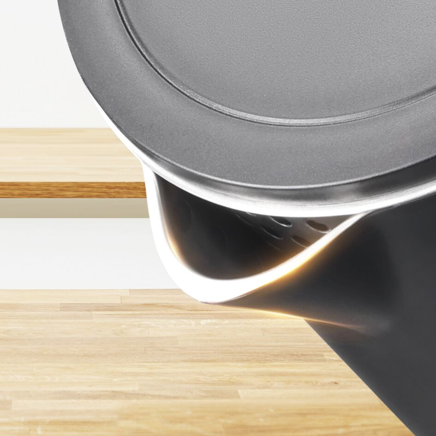 Close-up of a black kettle with a wooden surface and white wall in the background.