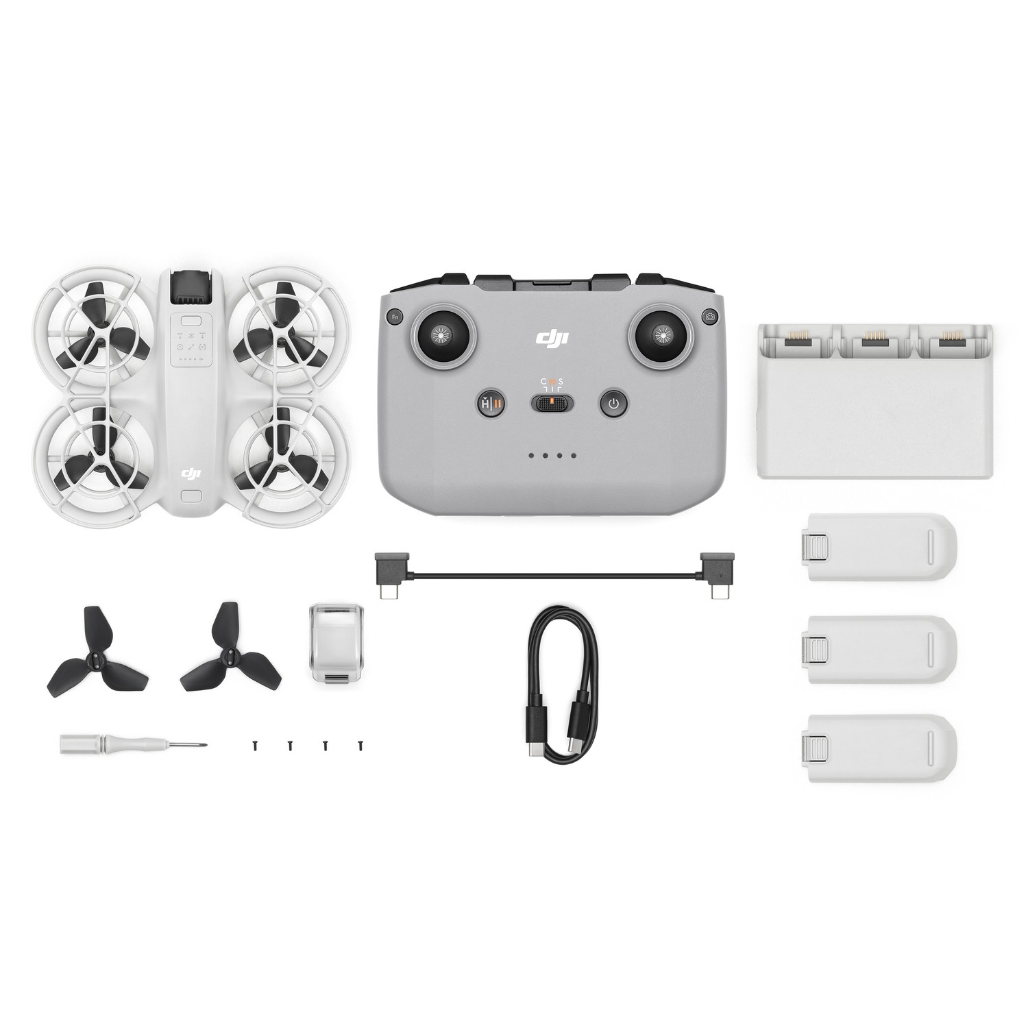 Kit de drone avec drone, télécommande, batteries et accessoires, disposés sur une surface blanche.