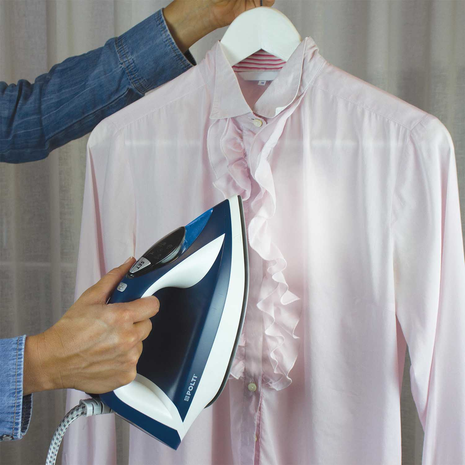 Una persona che stira una camicia rosa con volant su un'appendiabiti, con un ferro da stiro blu.