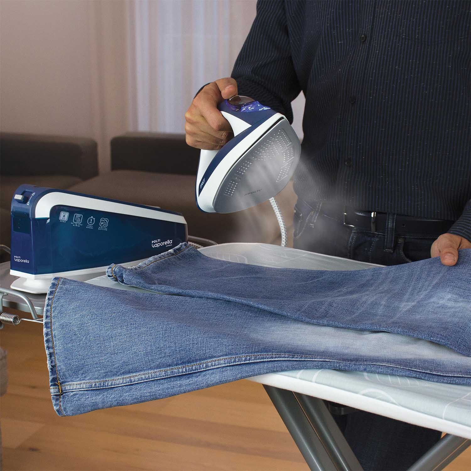 Uomo che stira jeans su asse da stiro con ferro a vapore. Secondo stiratore e denim.