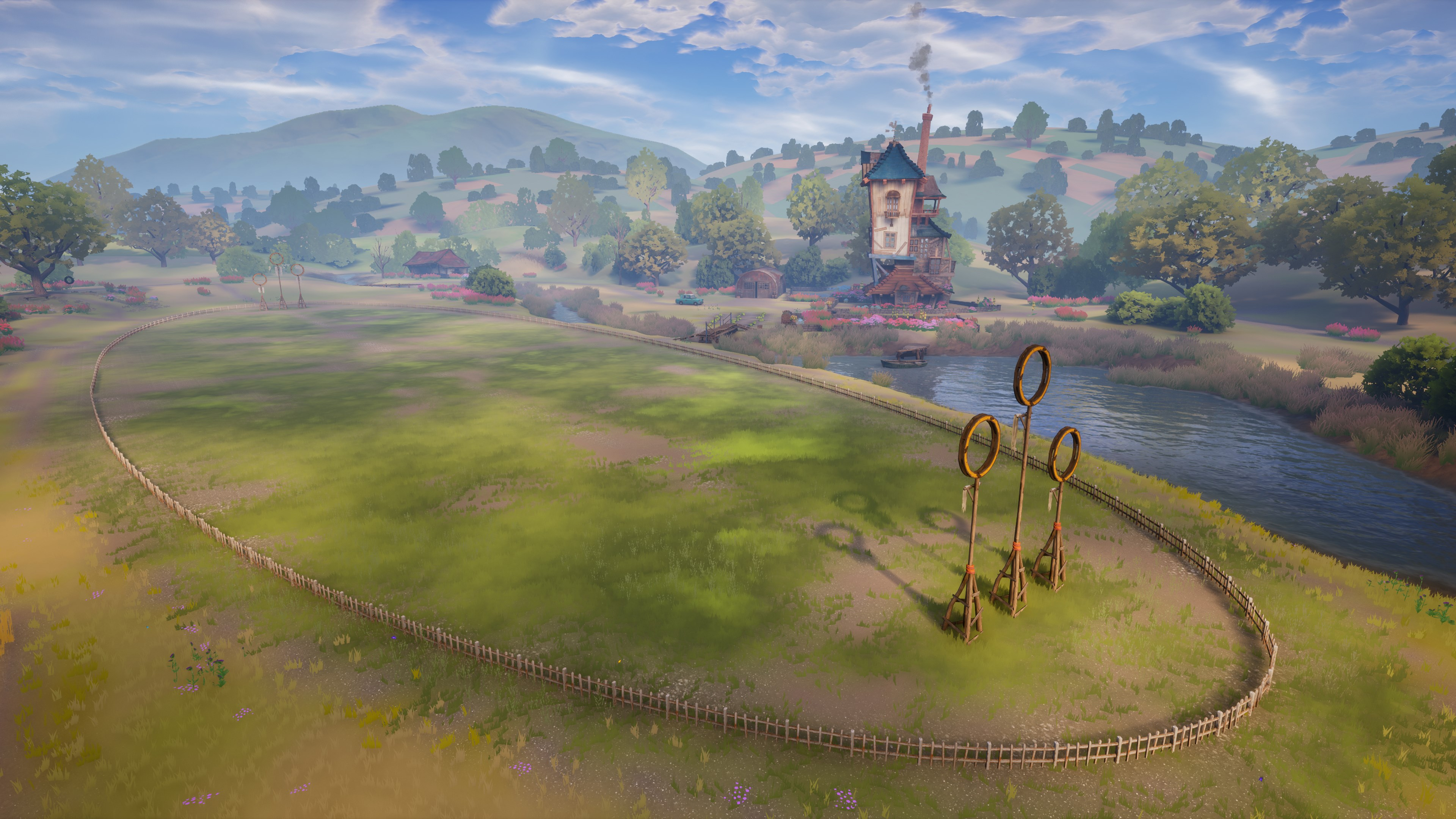Un terrain avec des buts de Quidditch, un bâtiment et une rivière. Un ciel bleu ensoleillé est au-dessus.