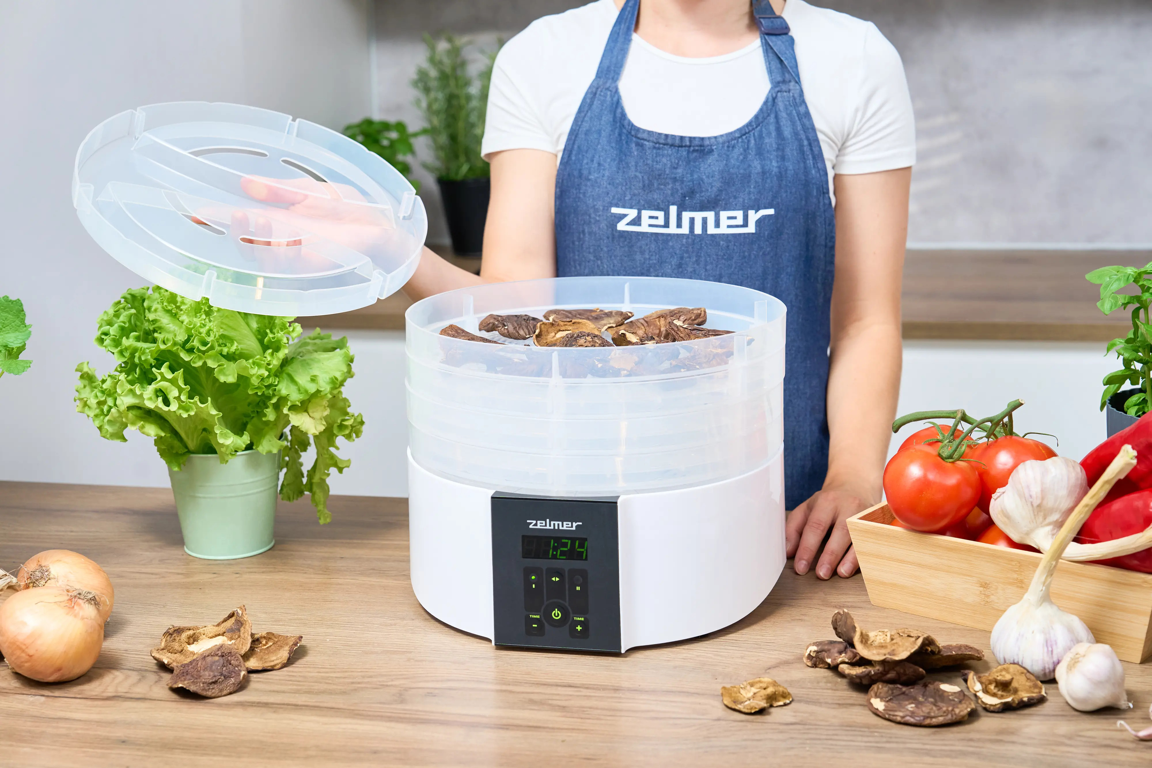 Kobieta zakłada pokrywę na suszarkę do żywności z jedzeniem i warzywami wokół.