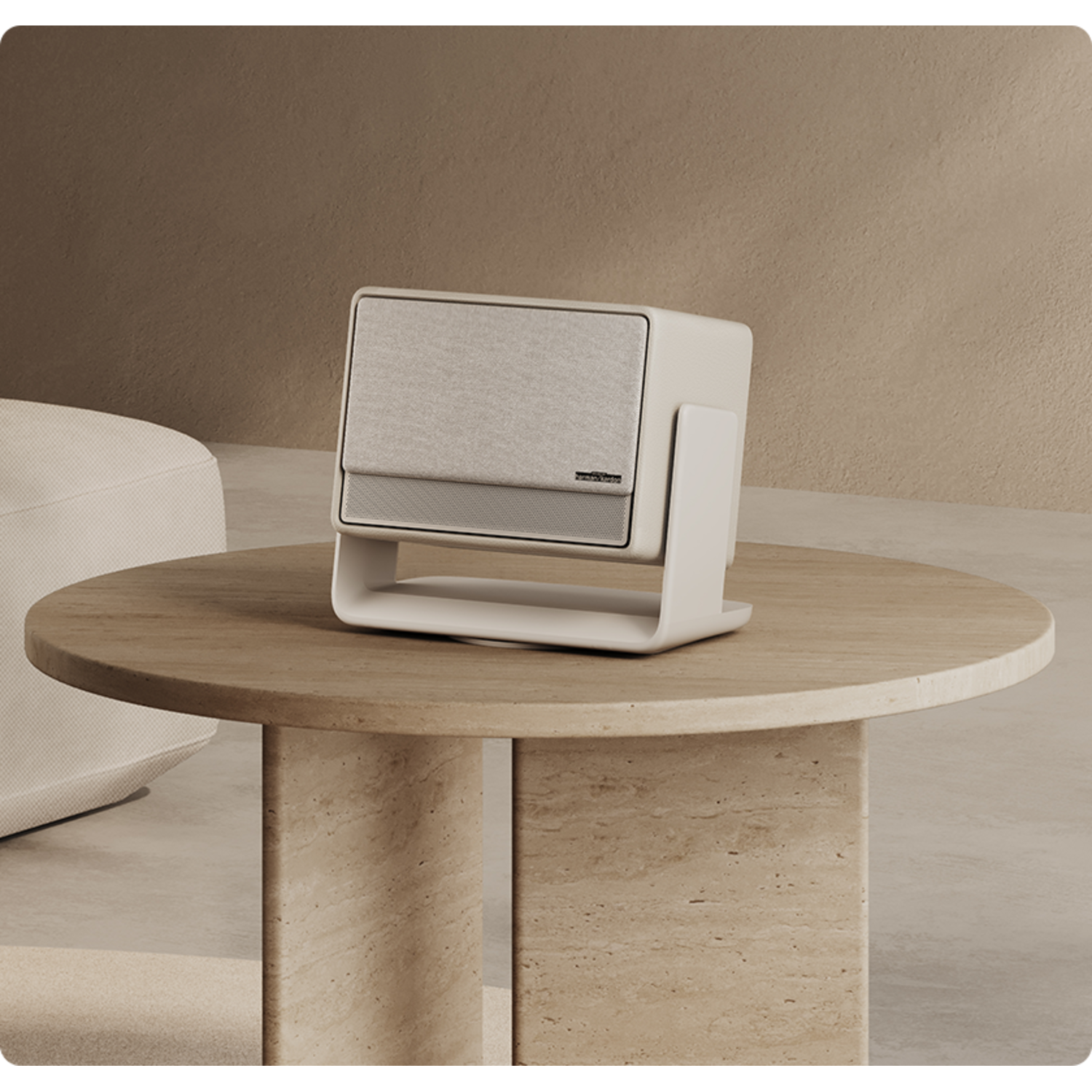 A modern white speaker with a fabric front sits on a round, light-colored table.