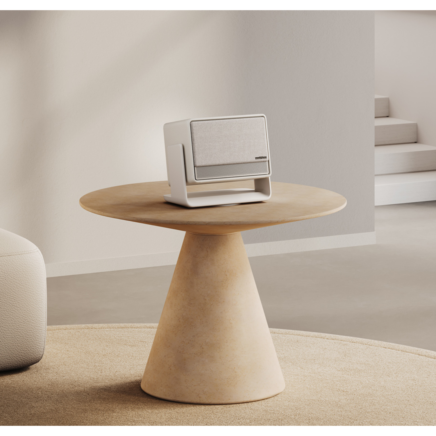 A white speaker is set on a light-colored table, in a well-lit room with carpet.