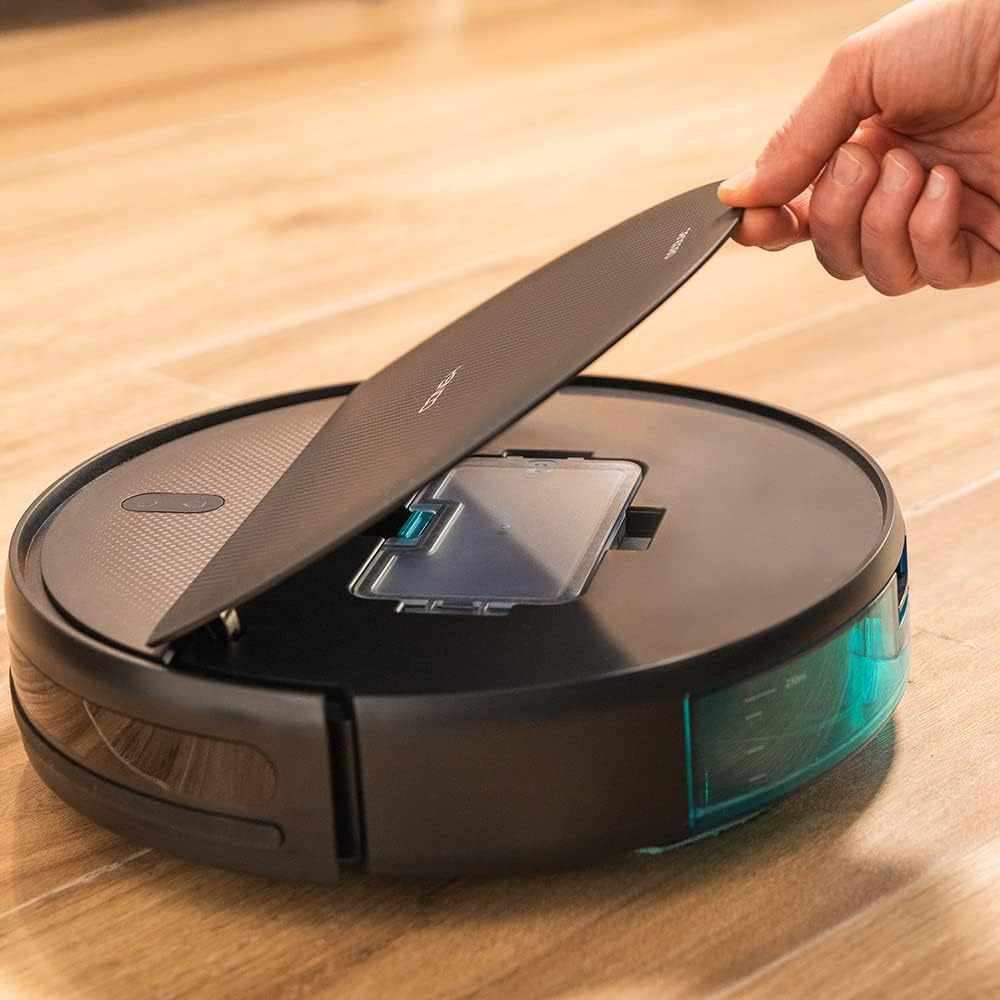 Egy kéz felemeli a fekete és türkiz robotporszívó fedelét egy fa padlón.
