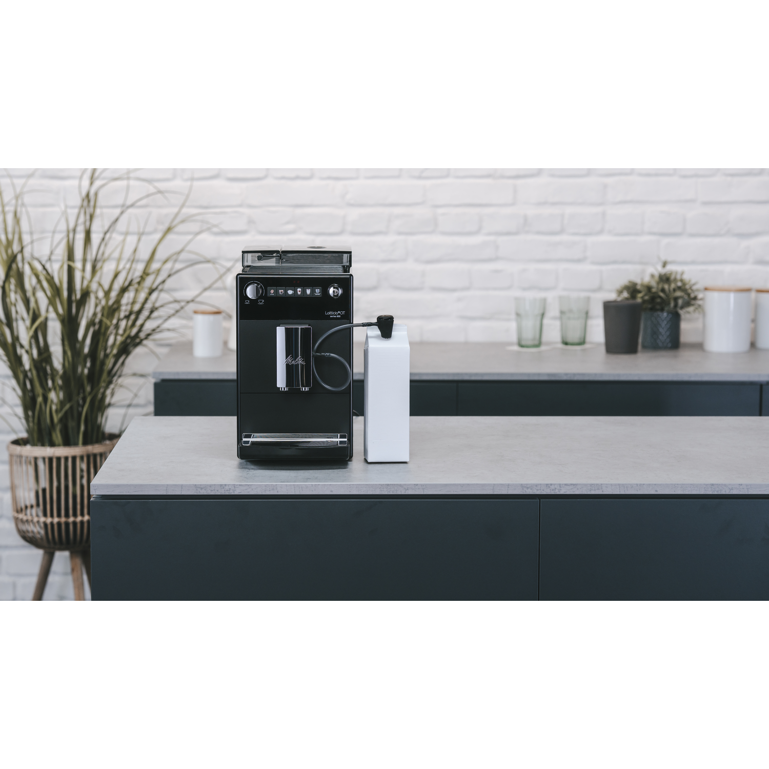 Black coffee machine with milk container, on a gray countertop with white brick wall.