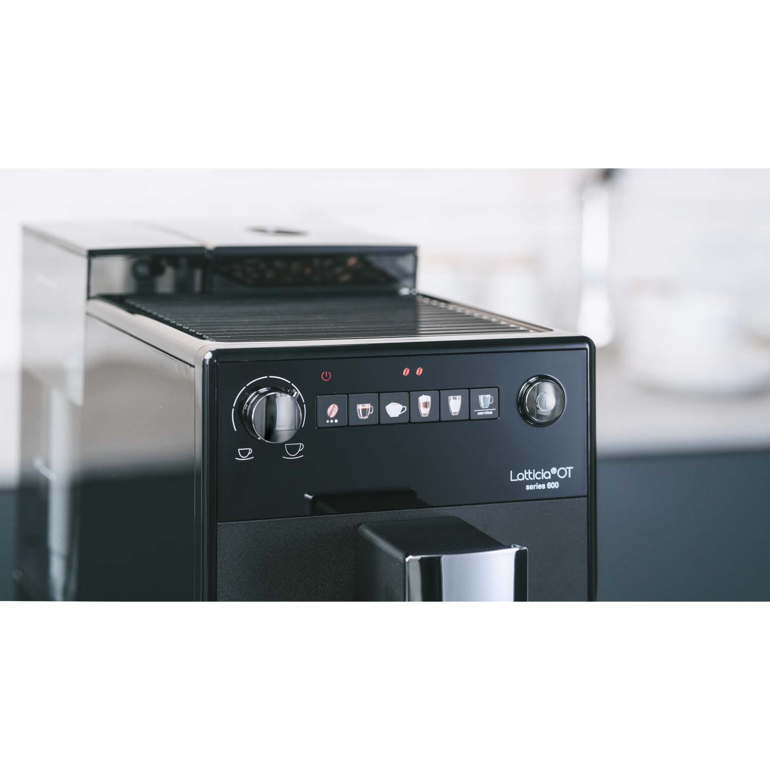 Espresso machine close-up. Black with buttons and display. Coffee beans visible on top.