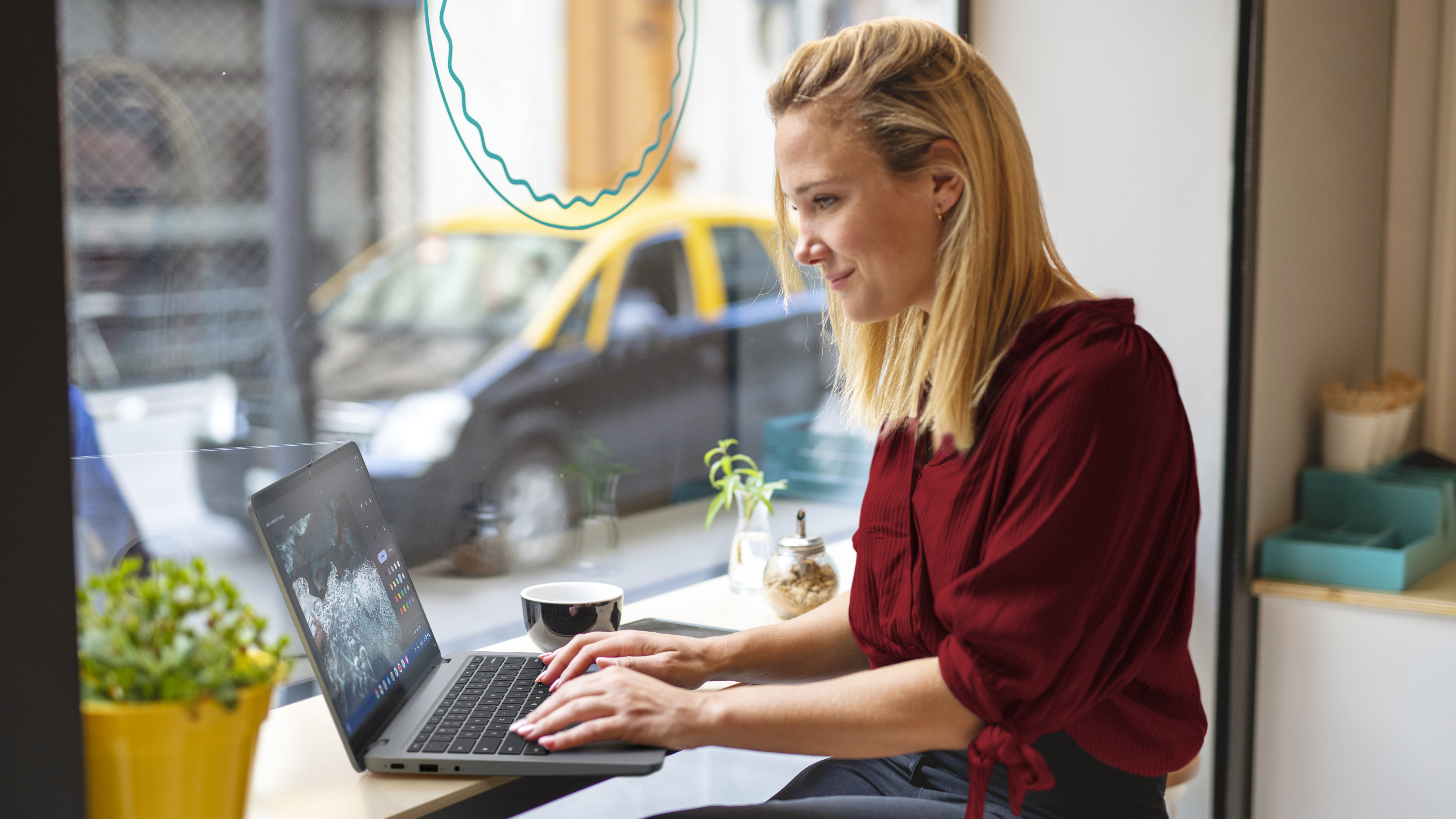 Frau arbeitet im Café an einem Laptop, in der Nähe eines Fensters mit verschwommenem Straßenblick.
