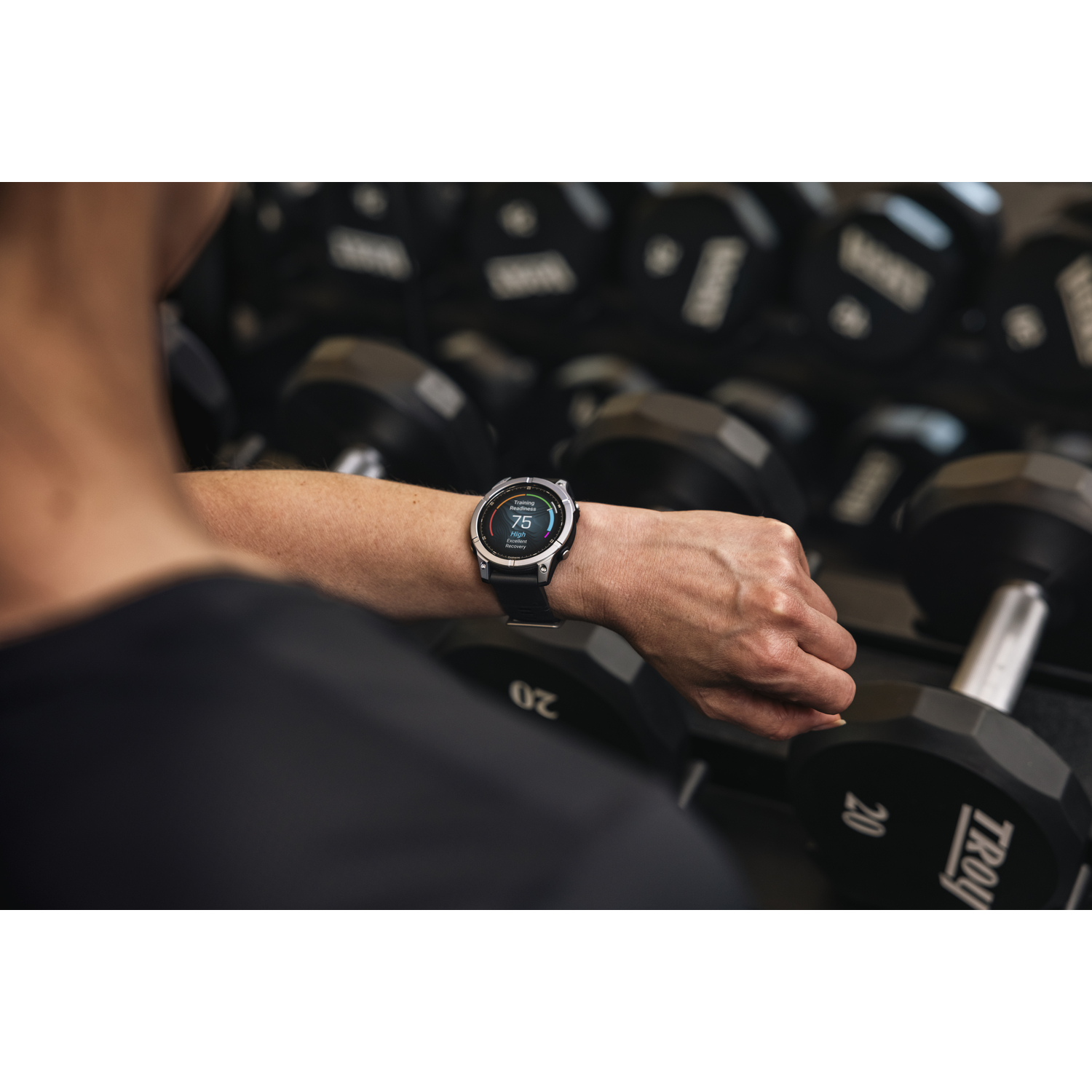 Een persoon met een smartwatch controleert trainingsgegevens. Halters op de achtergrond.