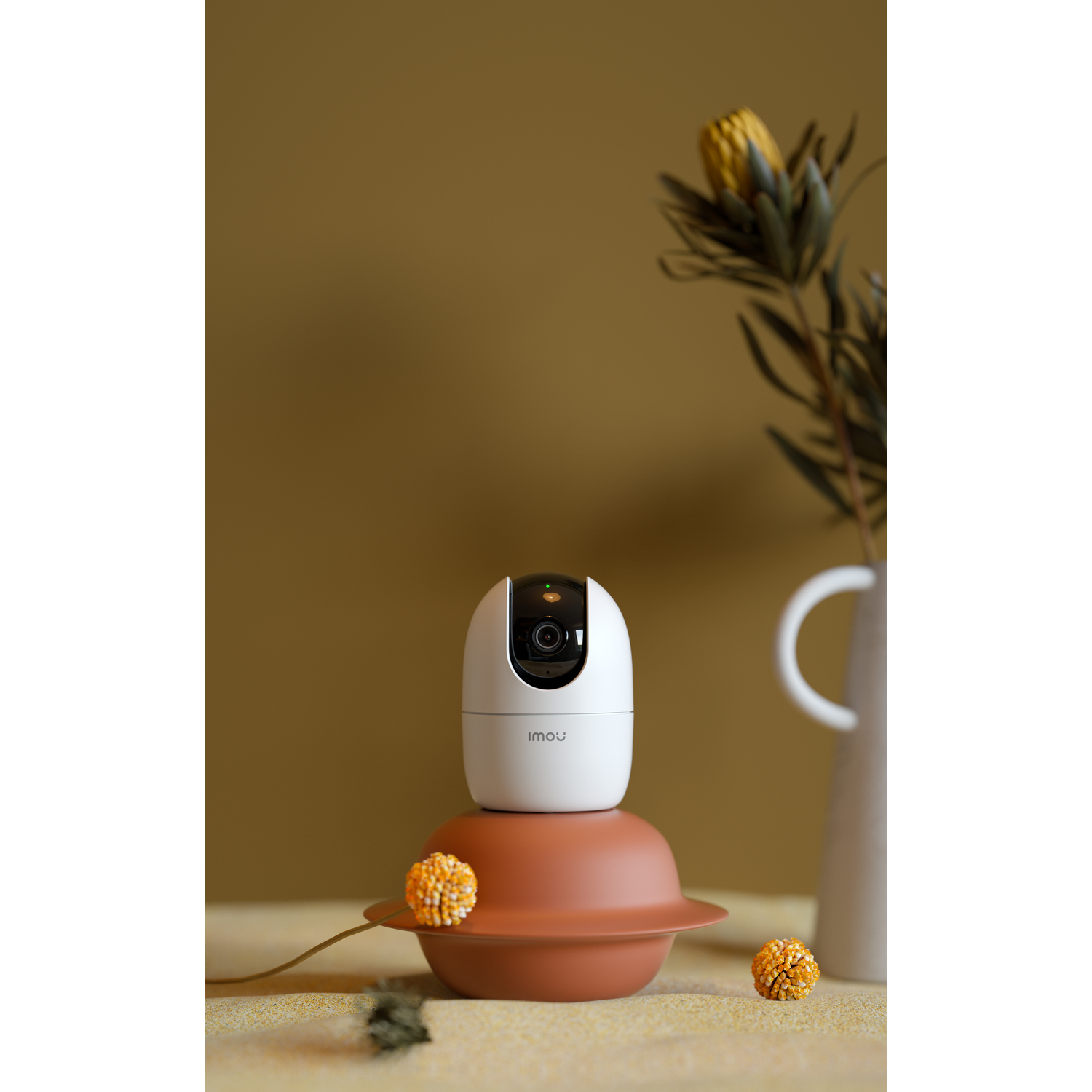 White and brown Imou security camera on a decorative stand with flowers.