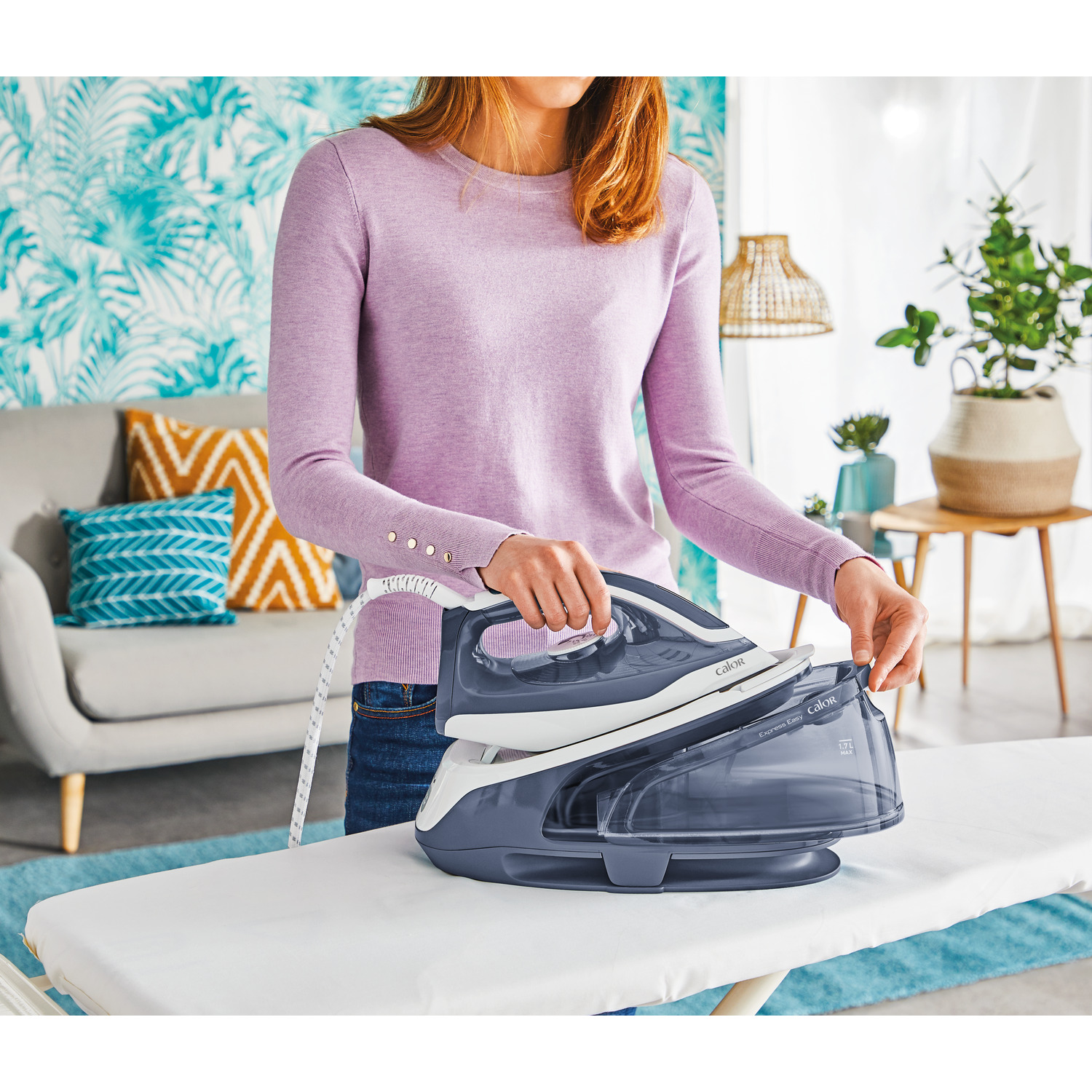 A woman ironing clothes on an ironing board. The iron is gray and white.