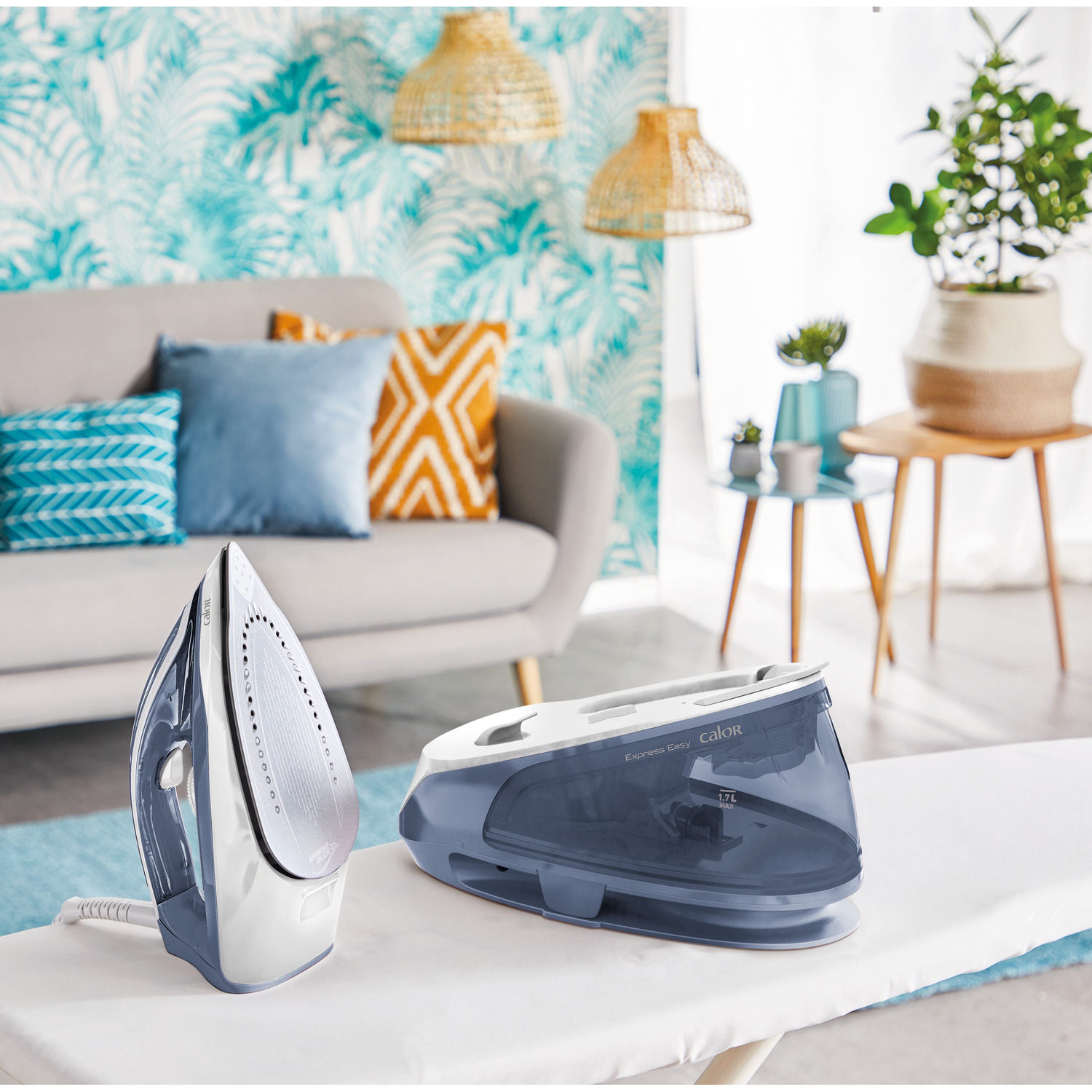 An iron and a water tank. They are on an ironing board in a room with a couch and decorations.