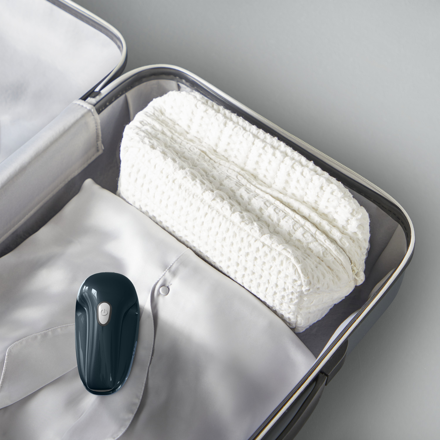 Valise ouverte avec une chemise blanche pliée, un sac blanc à motifs gaufrés et un appareil vert foncé.