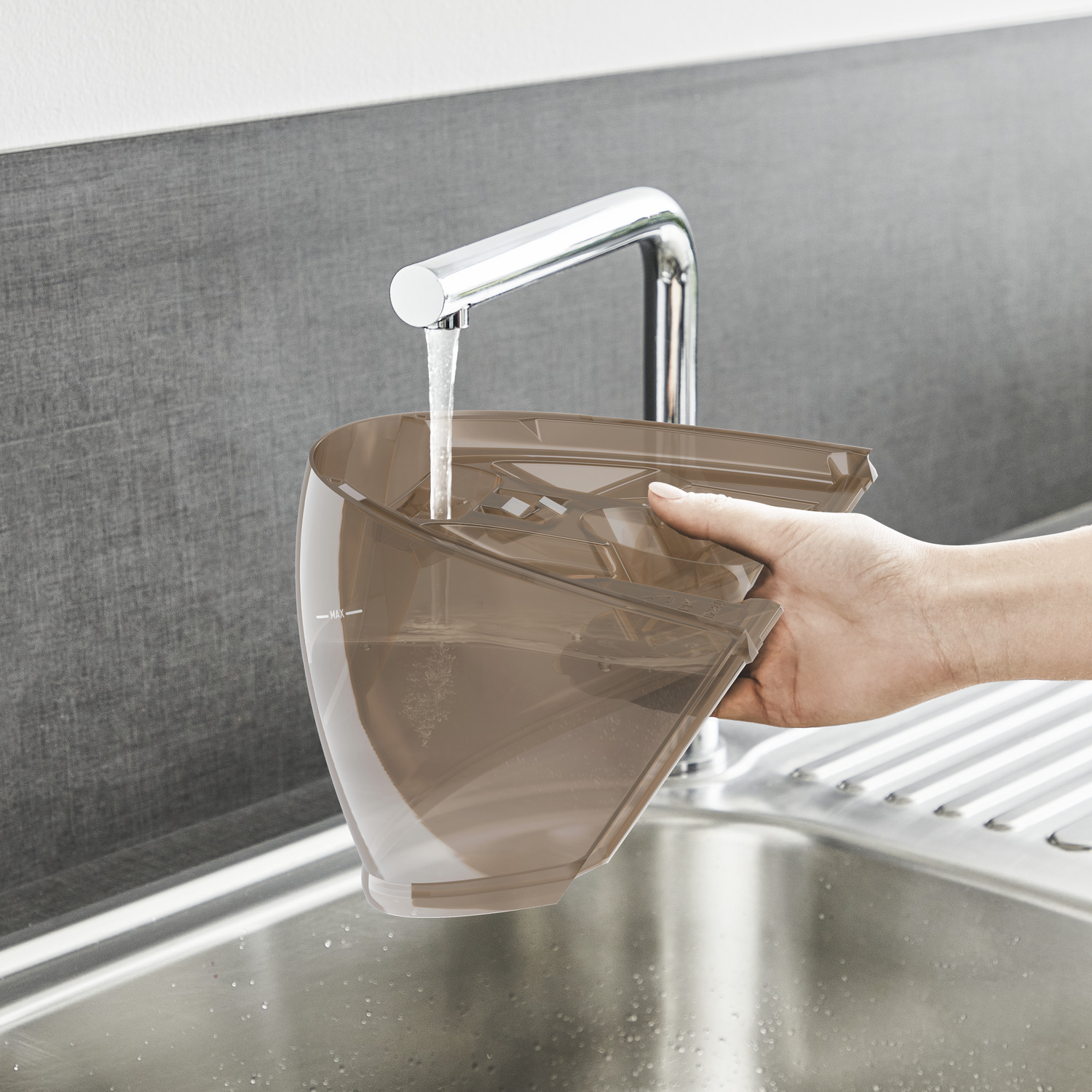 A hand fills a brown container with water from a faucet in a stainless steel sink.