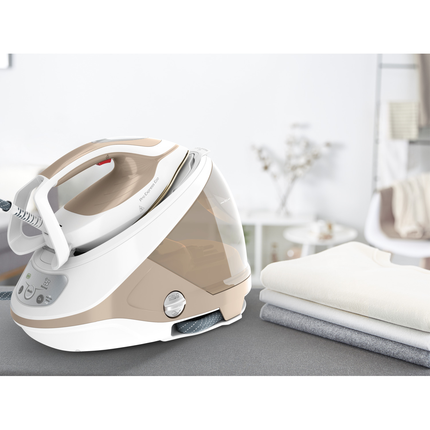 White and beige steam iron with a stack of folded clothing on a table.