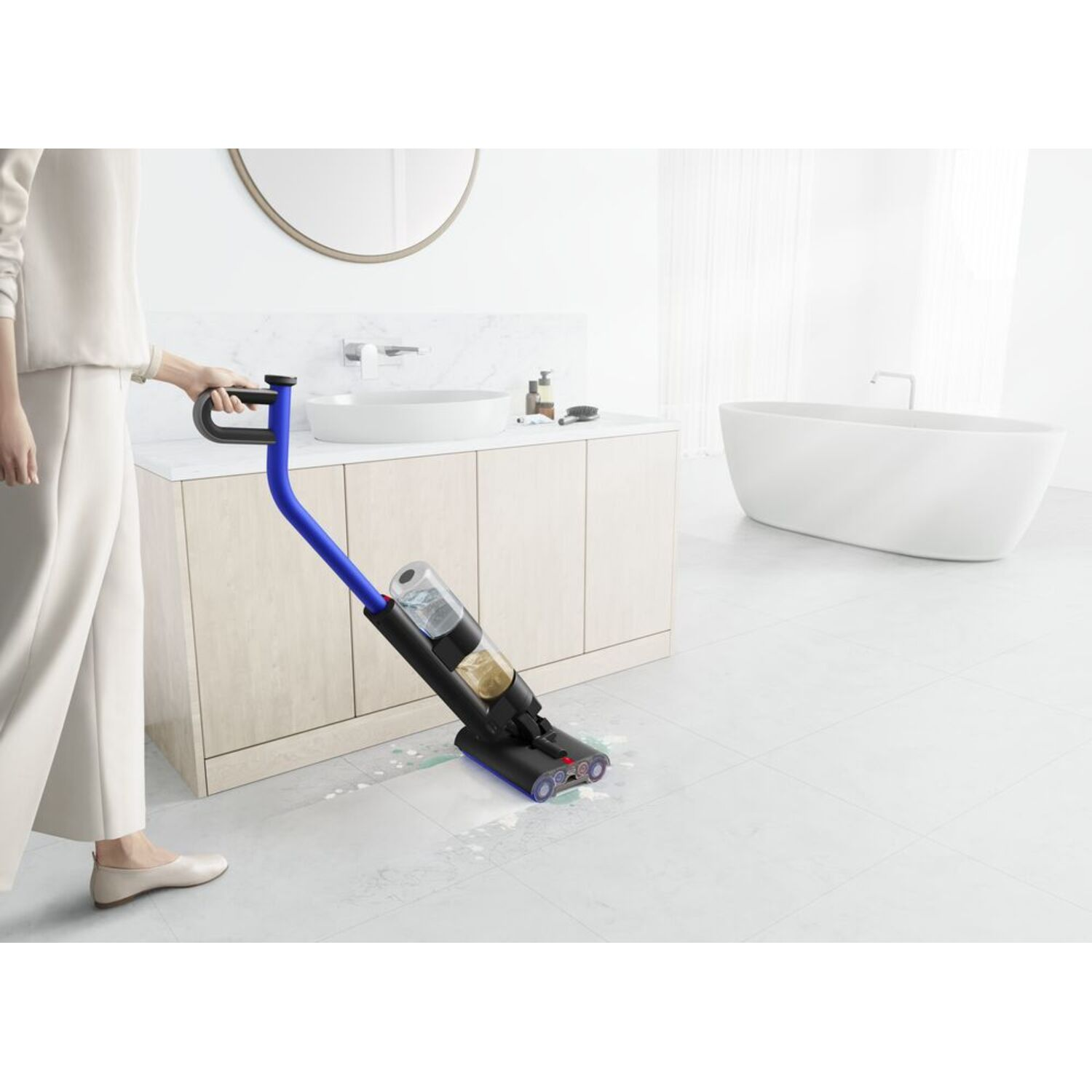 A woman vacuums a white tiled floor with a blue and black cordless vacuum. A white bathroom is in the background.