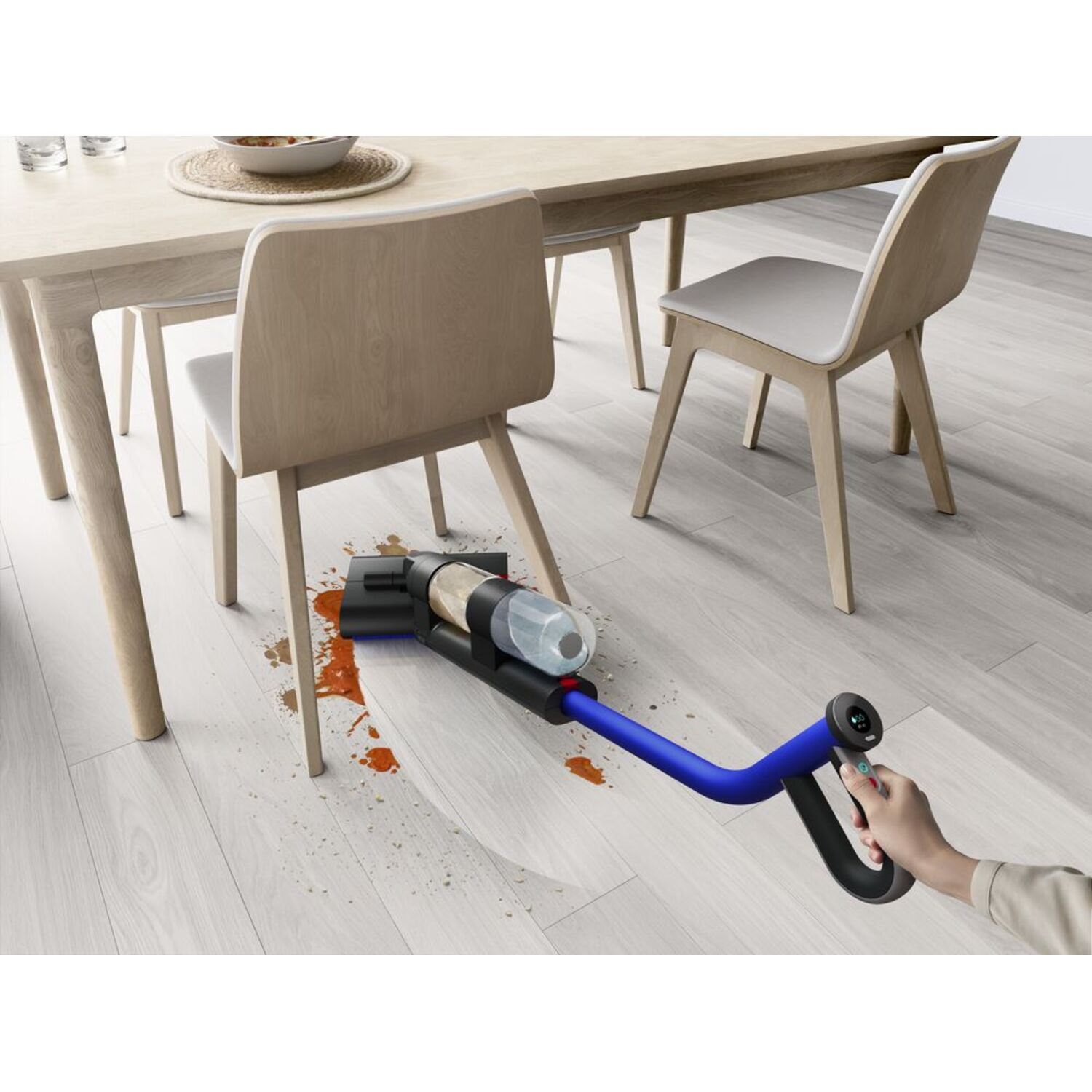 A person vacuums a spill on a light wooden floor with a cordless vacuum.