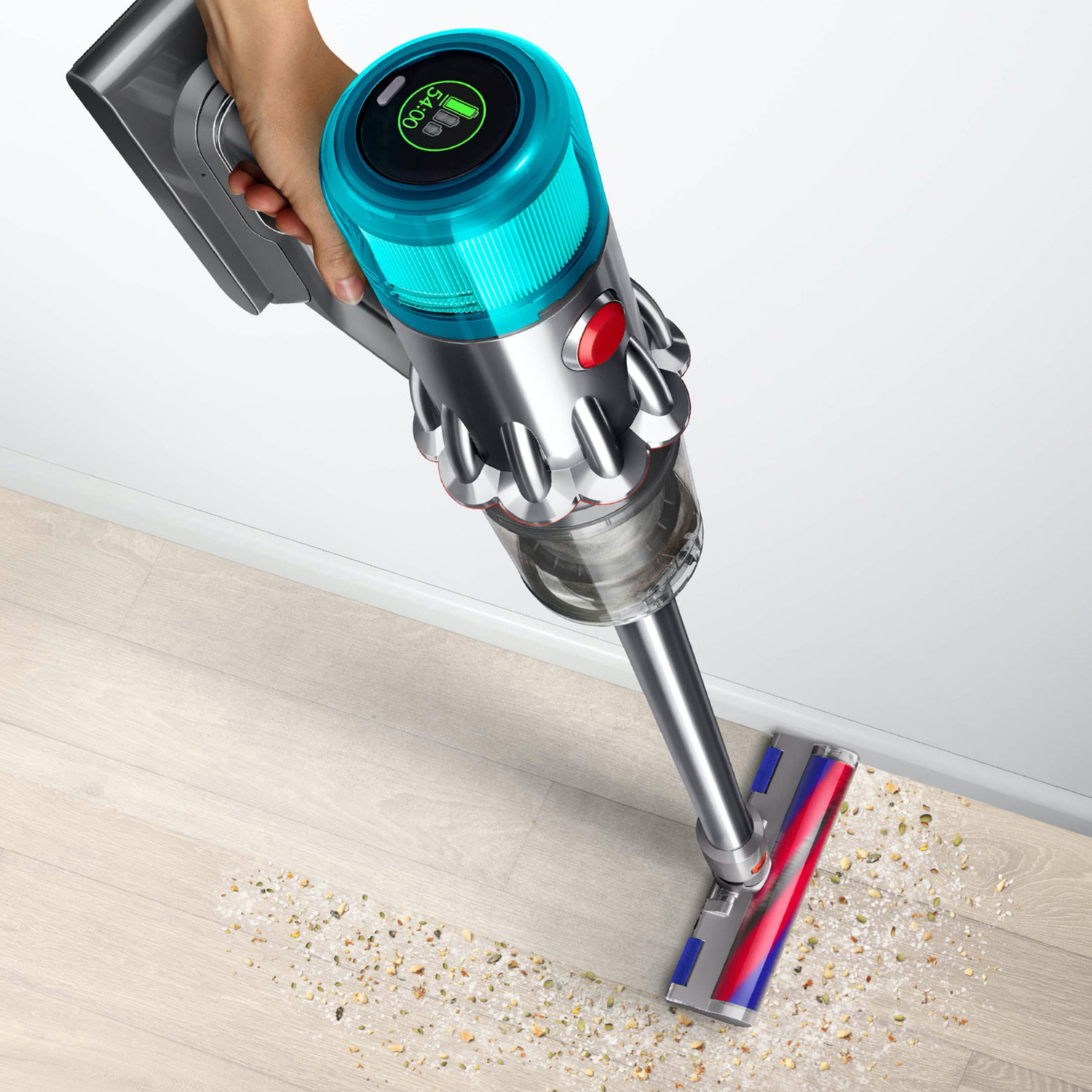 A person using a Dyson vacuum cleaner on a wooden floor, cleaning up debris.