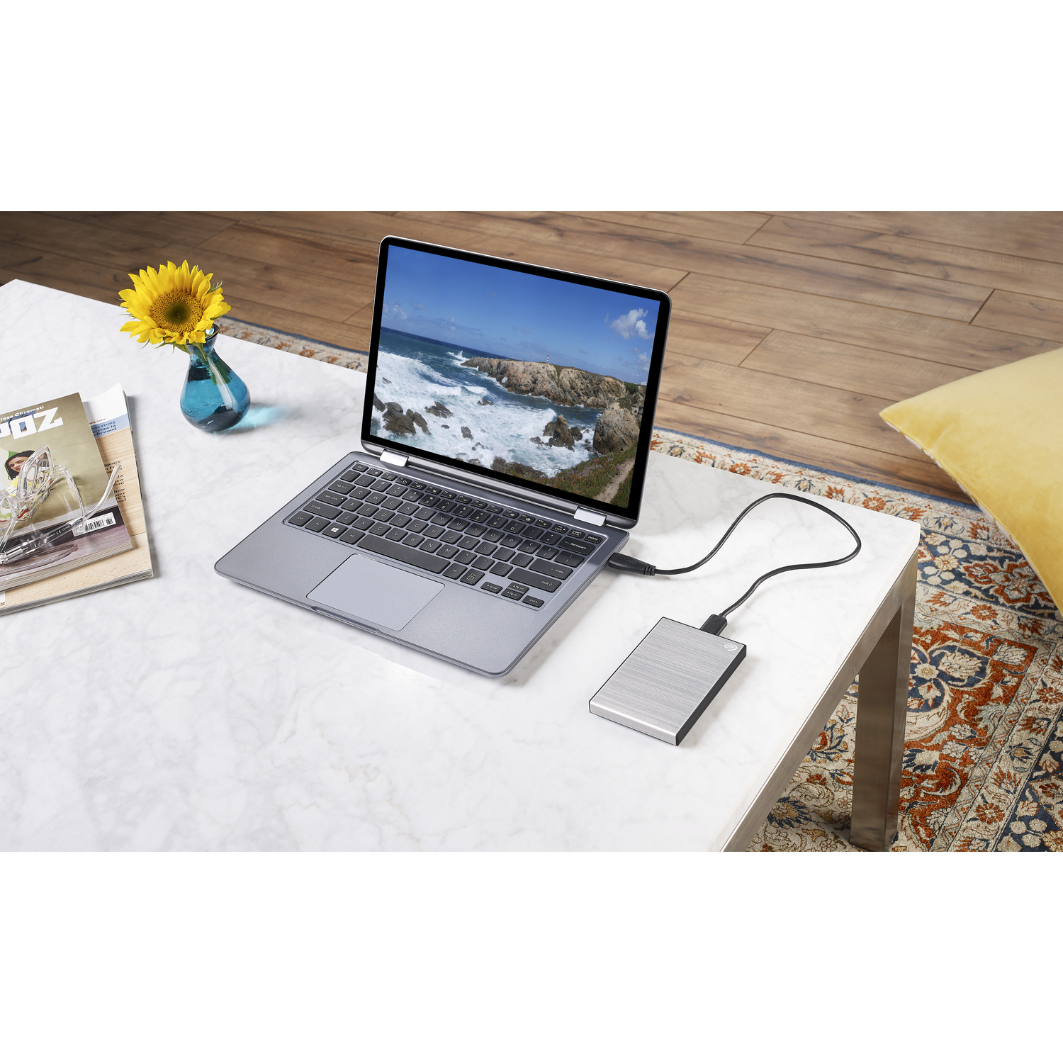 Ordinateur portable connecté à un disque dur externe sur une table en marbre, avec tournesol.