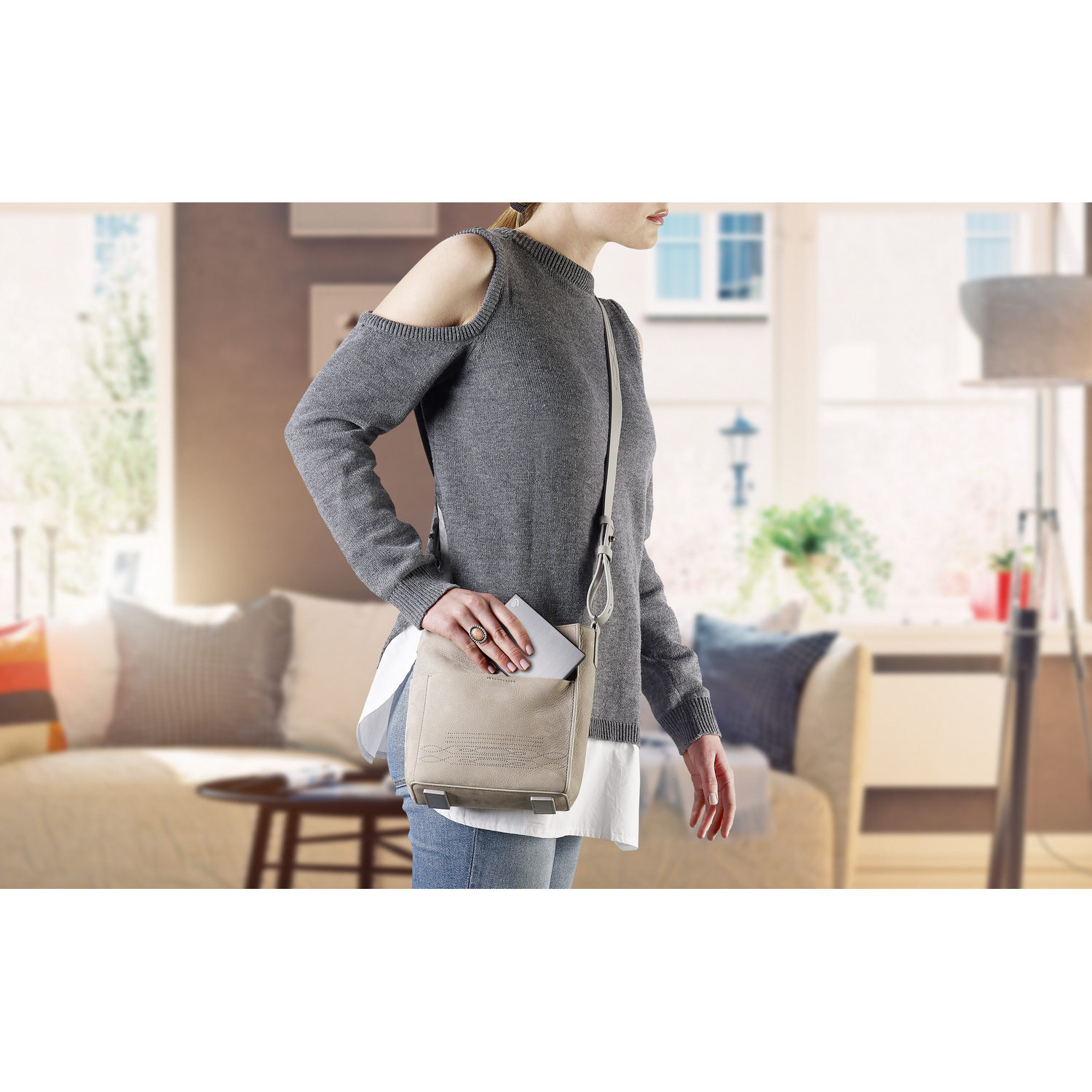 Femme avec un sac à main, pull gris. Montrant un salon en arrière-plan.