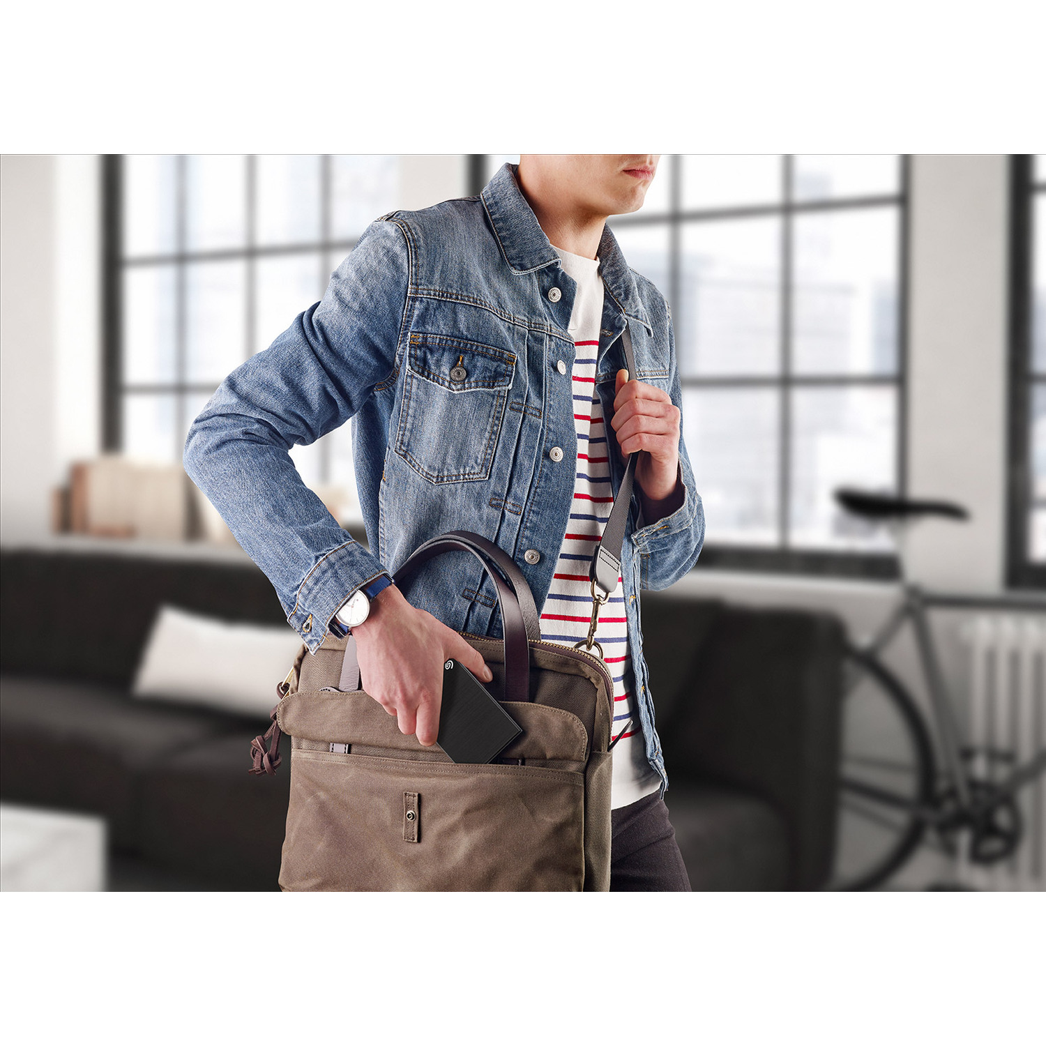 A man in a denim jacket reaching into a brown bag, inside a home.