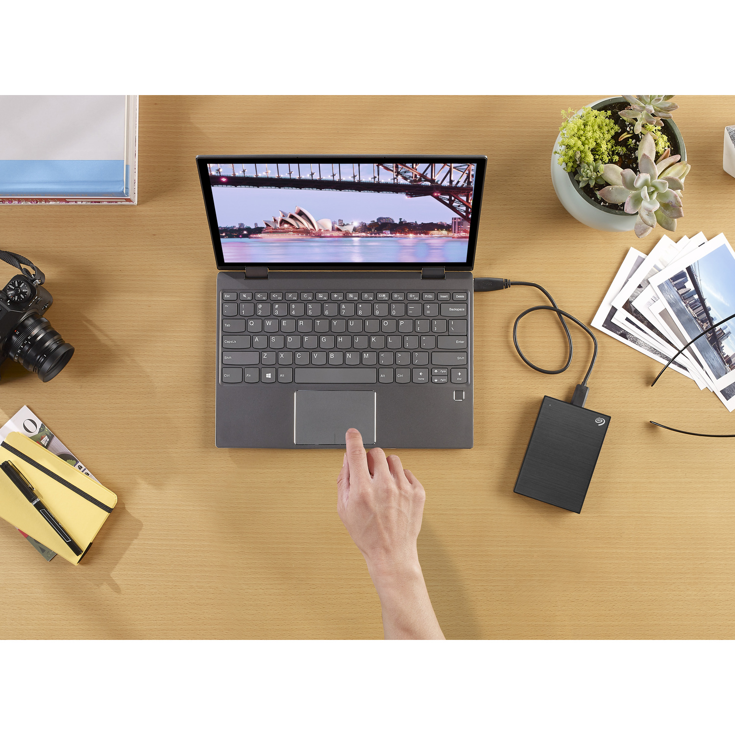 A laptop displaying a bridge image, external hard drive, and a person touching the screen.