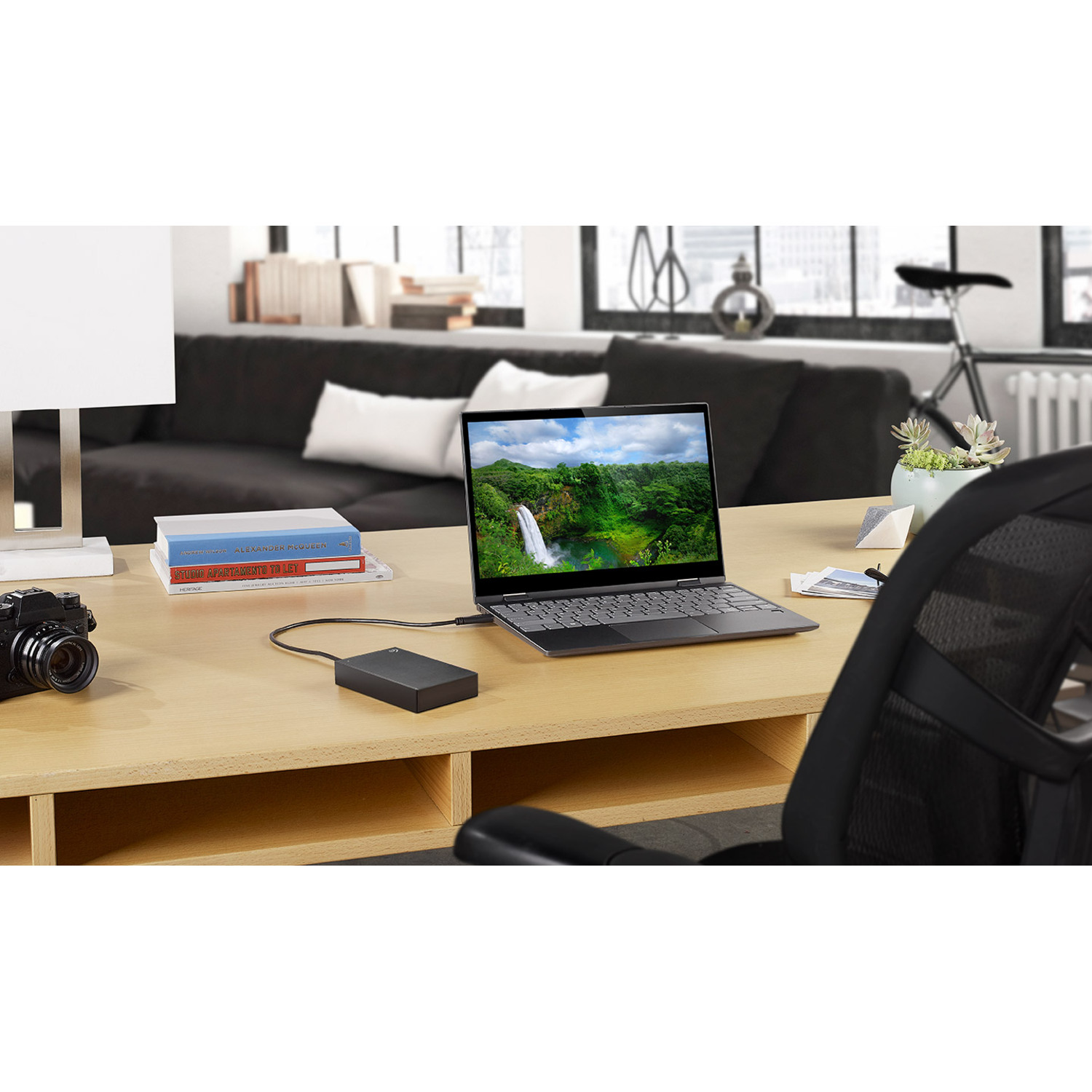 A laptop displays a waterfall scene, connected to an external hard drive on a desk.