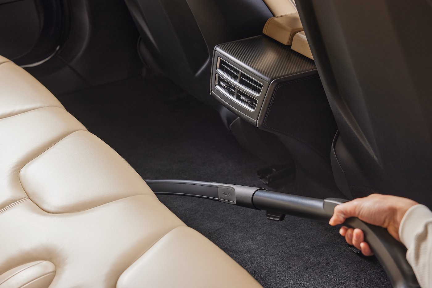 Eine Person, die den Rücksitz eines Autos mit beigen Sitzen und einer schwarzen Mittelkonsole absaugt.