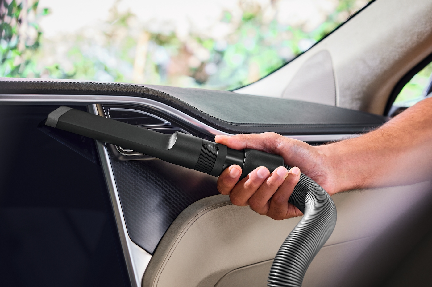 Eine Hand, die einen Staubsaugeraufsatz im Innenraum eines Autos verwendet.