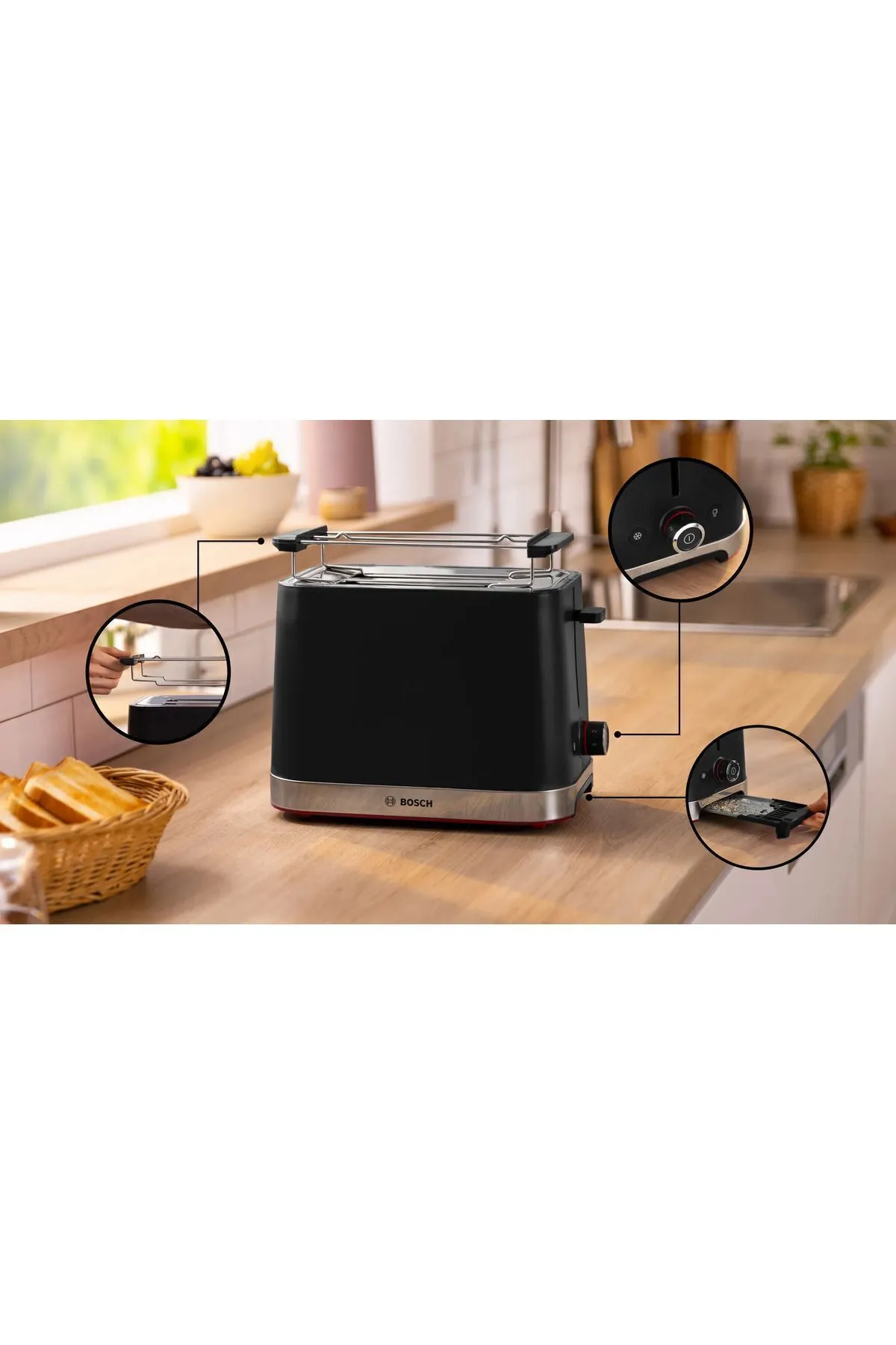 Kırmızı detaylı siyah bir Bosch tost makinesi ahşap bir tezgahta duruyor. Tost ve bir meyve kasası yakınlarda.