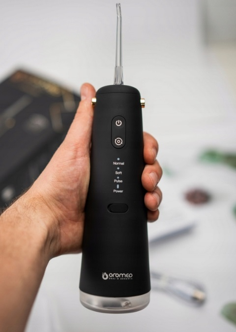 Czarny irygator do jamy ustnej, trzymany w dłoni. Przyciski i ustawienia widoczne na urządzeniu.