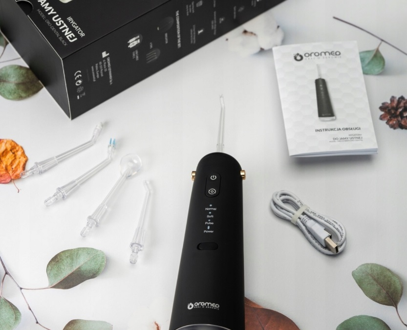 Czarny zestaw irygatora do jamy ustnej z końcówkami, pudełkiem i instrukcją na powierzchni zdobionej liśćmi.