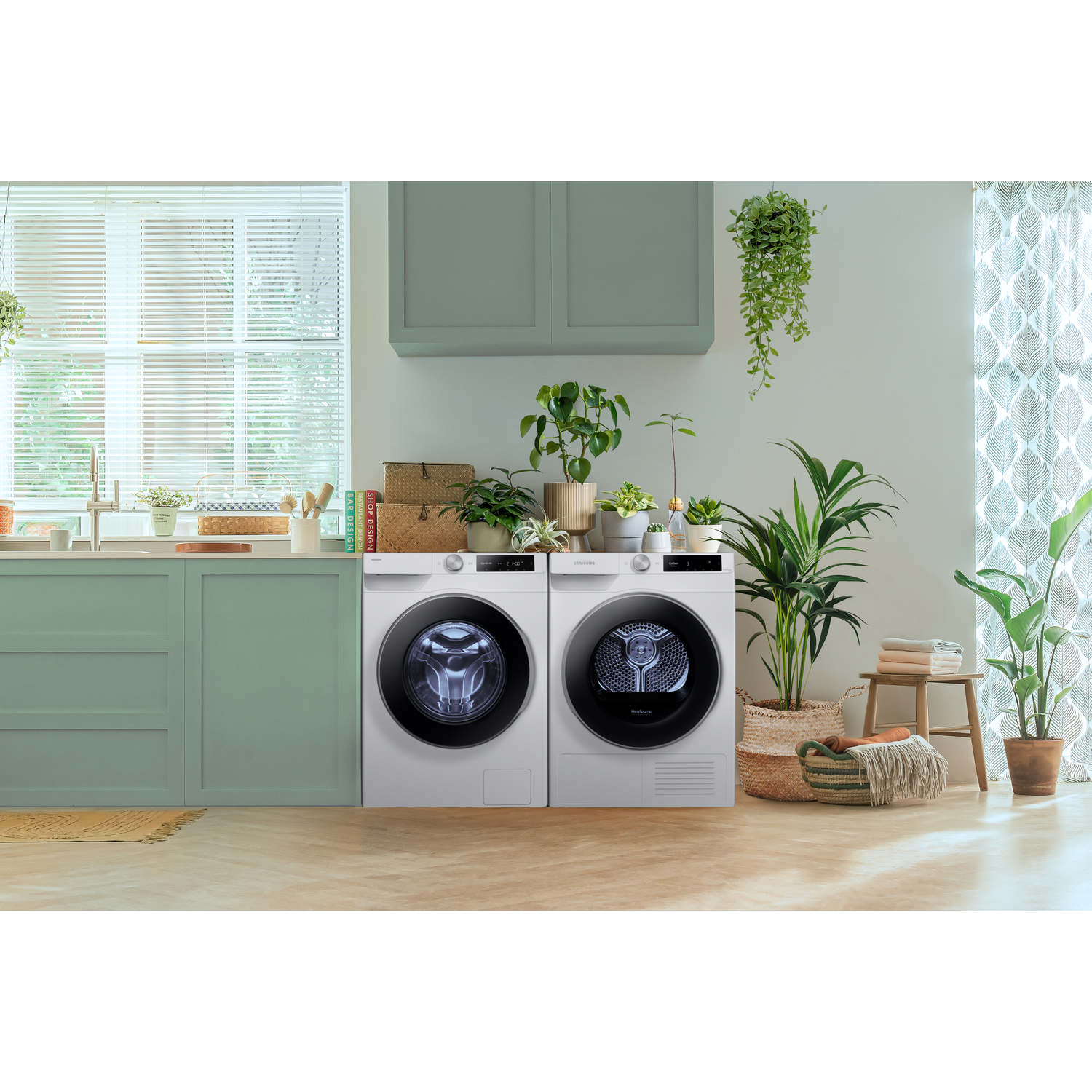 White washer and dryer set in a laundry room with plants, wooden stool, and a window.