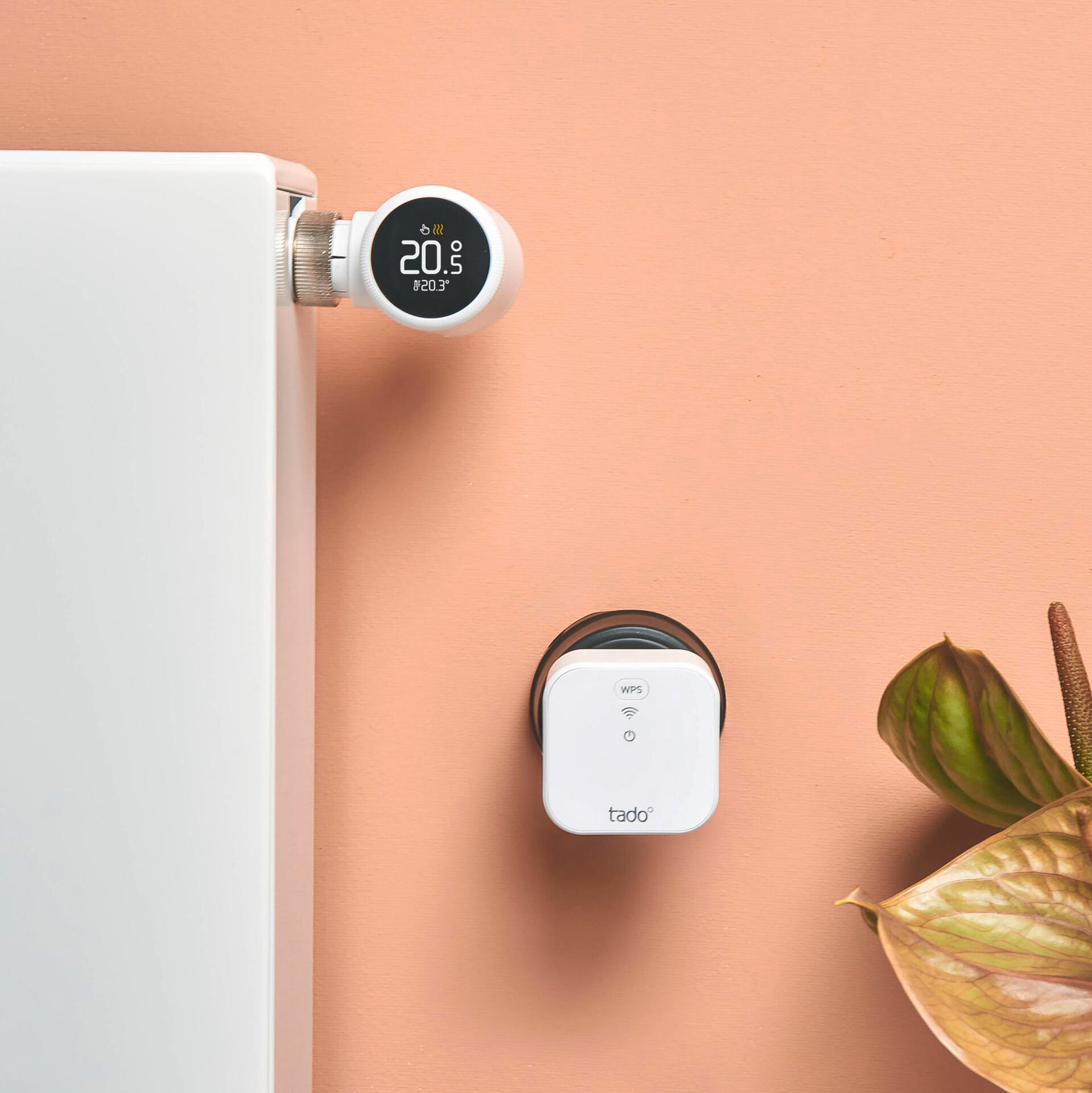 Smart-Thermostat an einem Heizkörper, mit weißer Steuerbox an der Wand daneben.