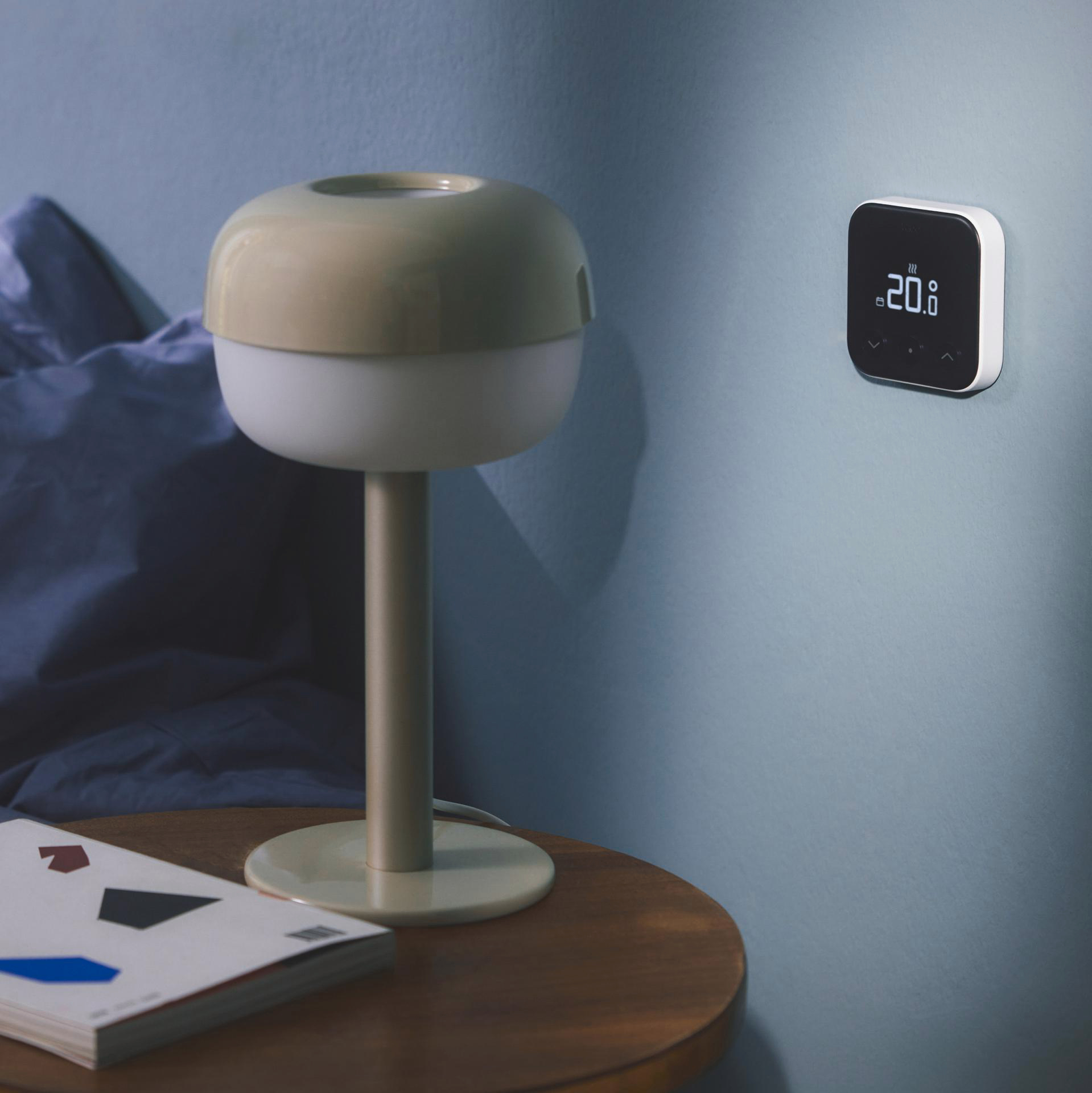 Eine Lampe und ein Thermostat an der Wand, mit einem Buch auf einem Tisch.