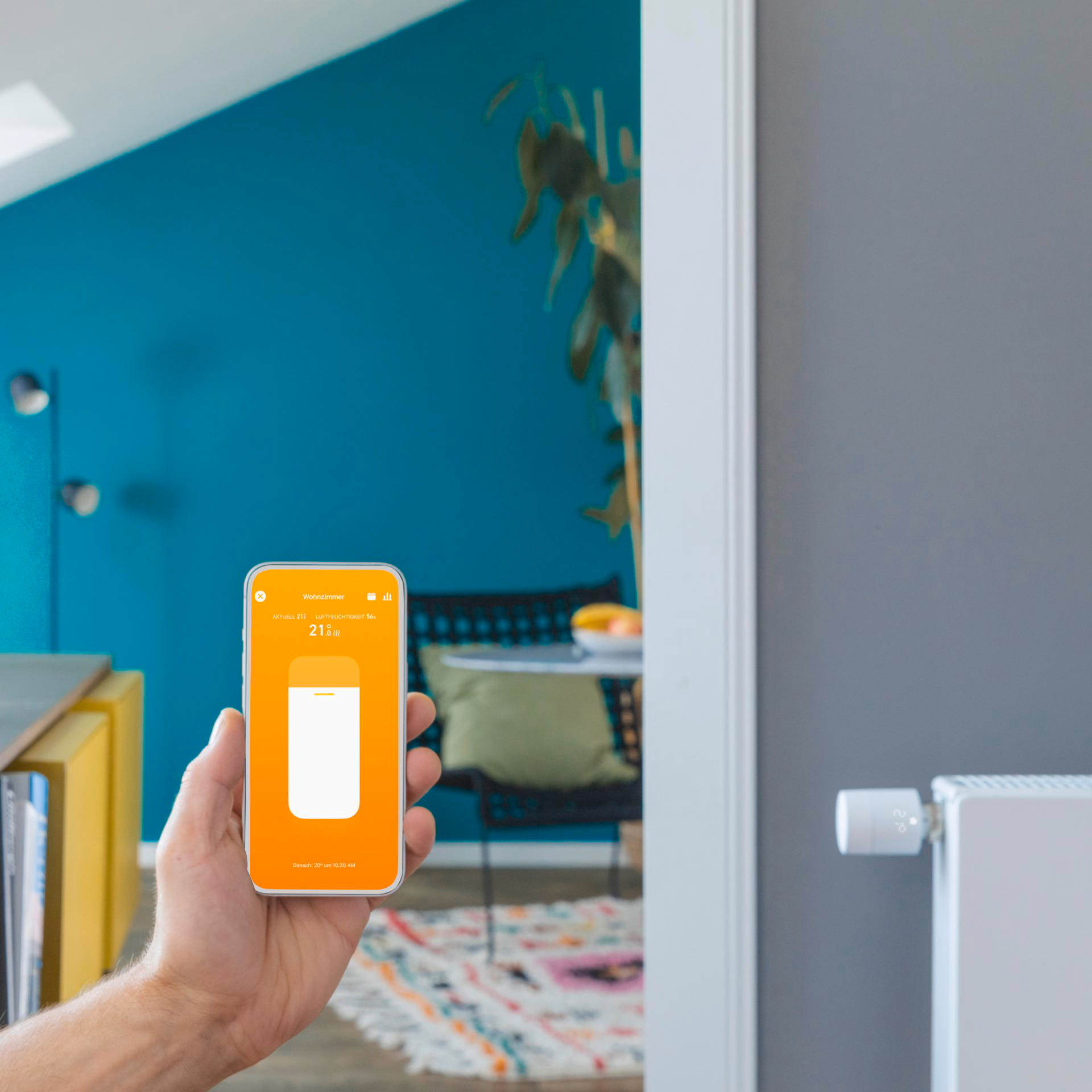 Eine Hand, die ein Smartphone mit geöffneter App-Oberfläche hält, neben einem Heizkörper.