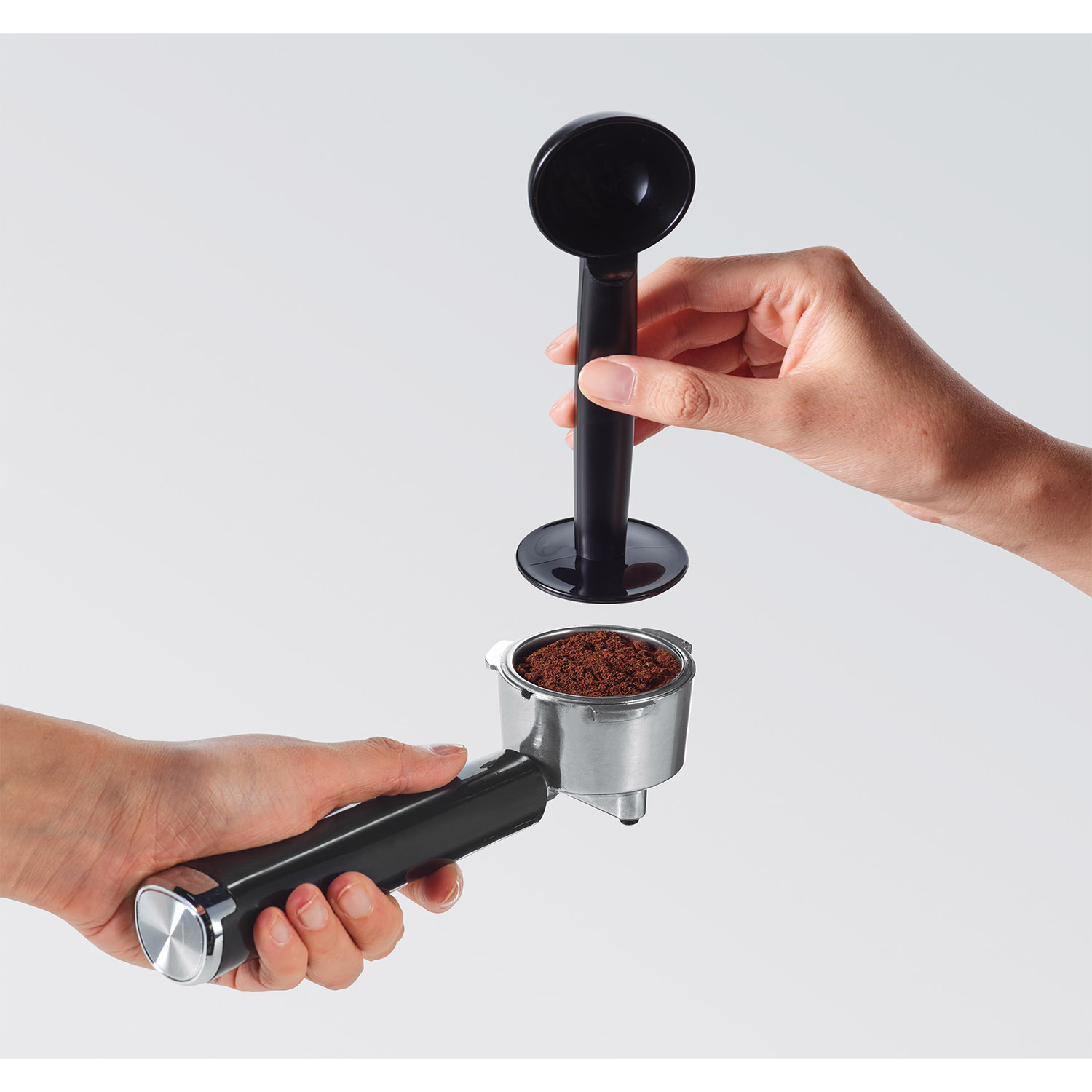 Mani che tengono parti di macchina espresso, preparandosi ad usarla. Sfondo bianco.