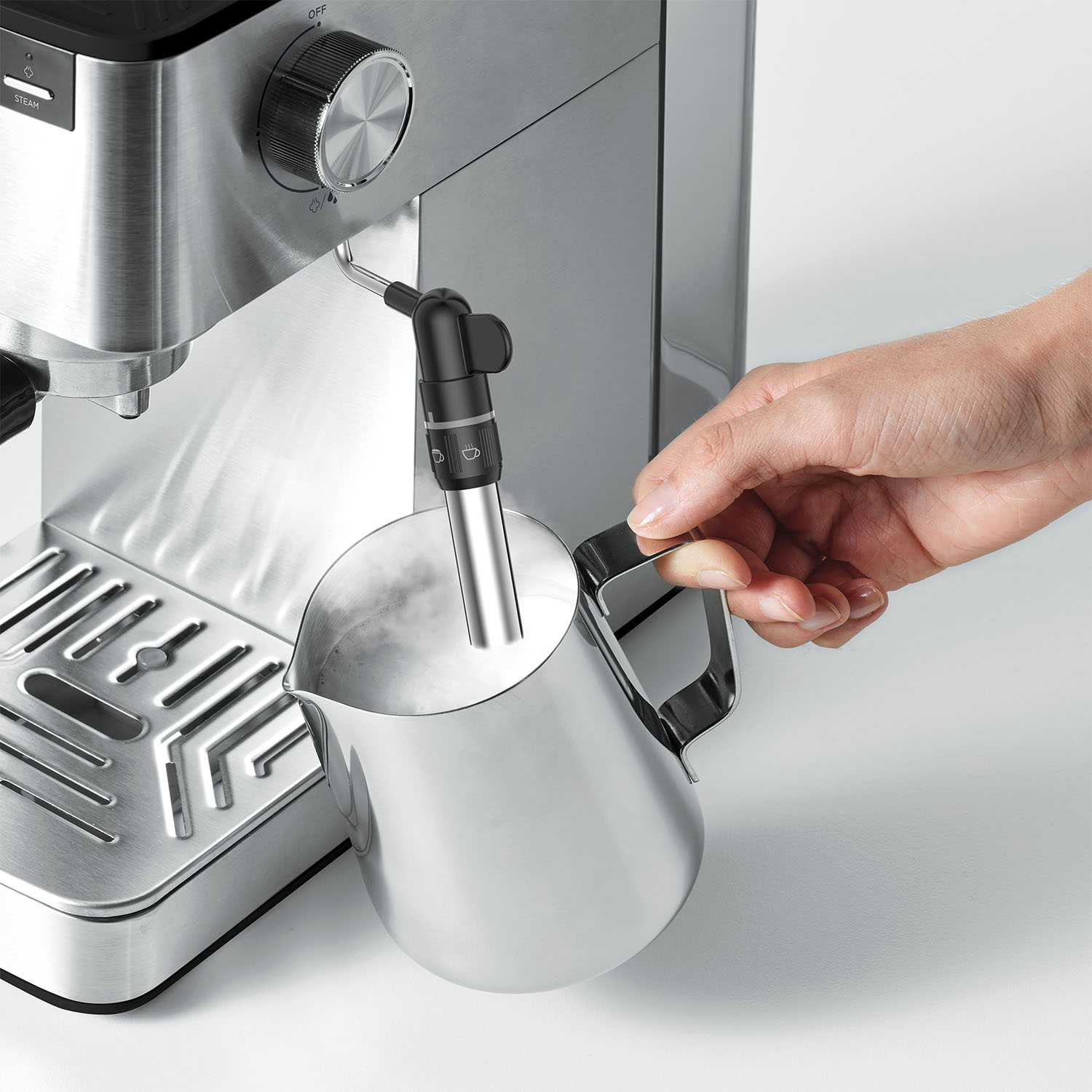 Una persona usa una macchina per espresso. Una brocca di metallo viene tenuta sotto la lancia vapore. Il vapore sale dal latte.