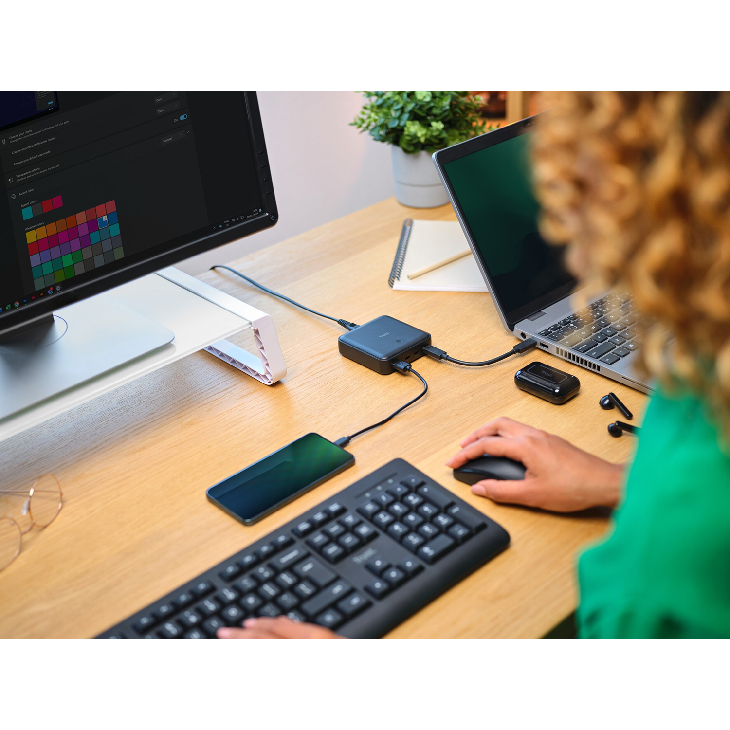 Persona alla scrivania con laptop, monitor, tastiera, mouse e telefono collegati a un hub.